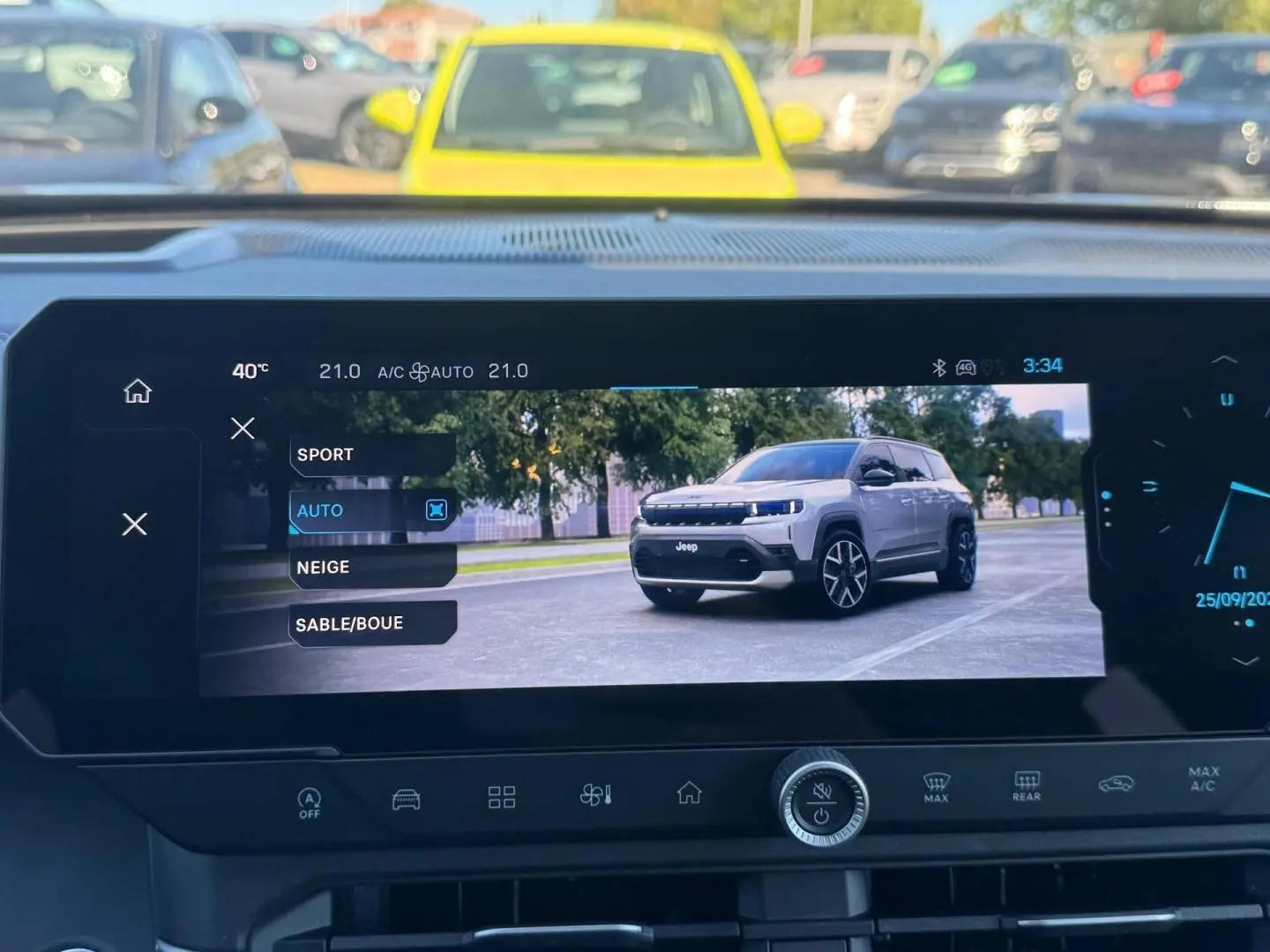 Écran tactile intérieur montrant un Jeep Compass gris en 3/4 avant sur route urbaine, avec arbres en arrière-plan.