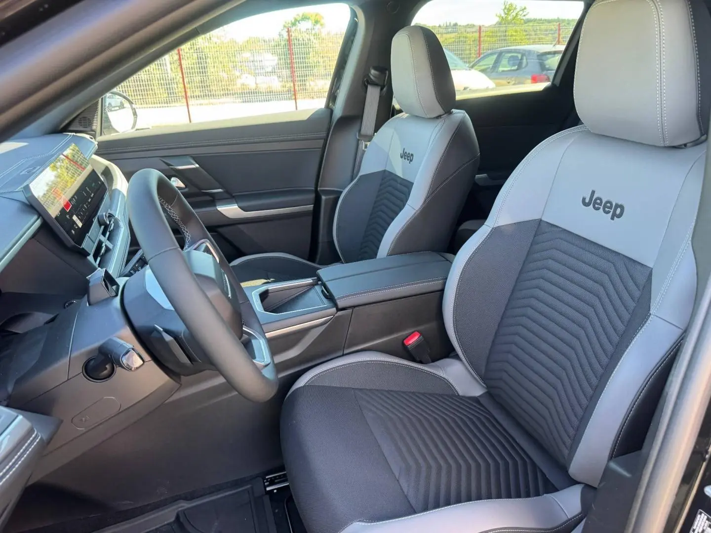 Vue intérieure côté conducteur du Jeep Compass 2026, sièges gris clair et noir avec logo Jeep brodé.