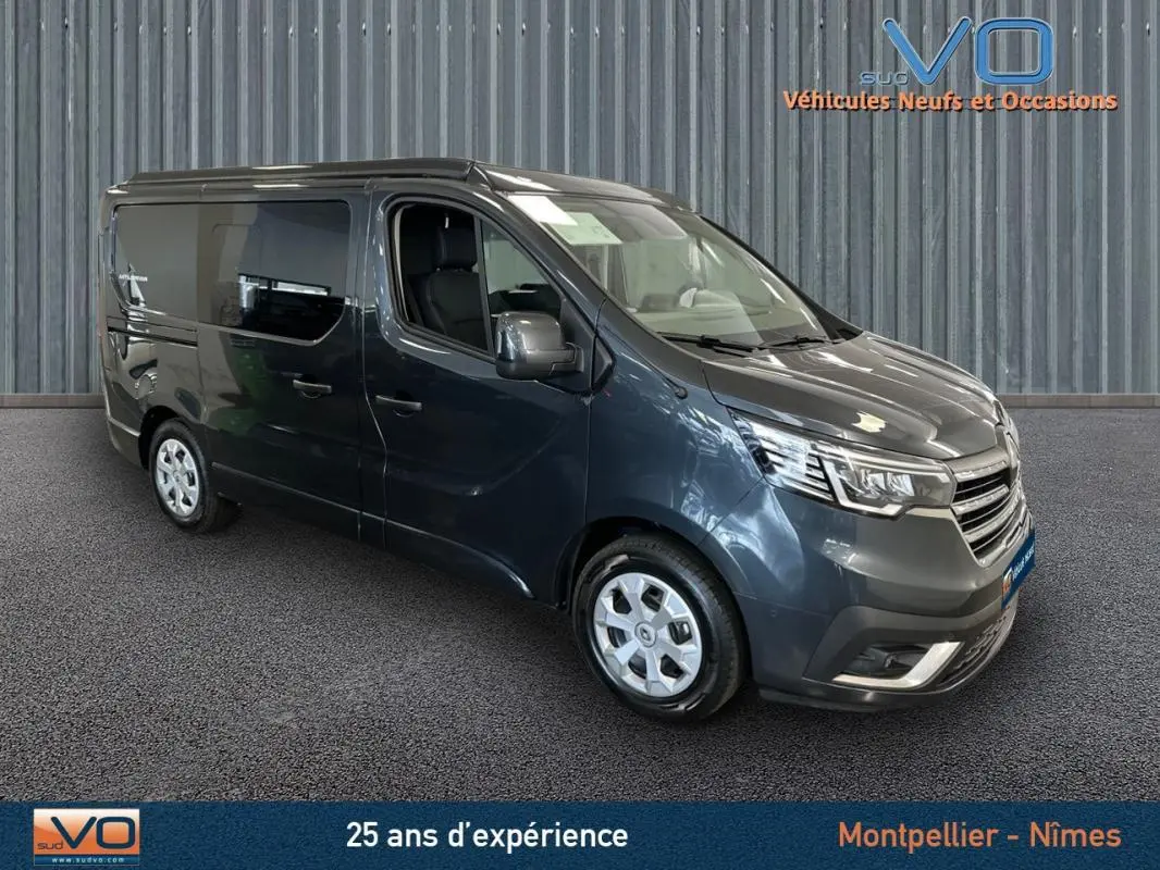 Renault Trafic Fourgon gris en 3/4 avant droit, vitres surteintées et jantes argentées visibles sur fond neutre.