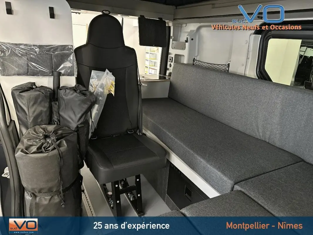 Intérieur du Renault Trafic Fourgon 2025 gris, vue sur siège passager et banquette avec rangements et équipements modulables.