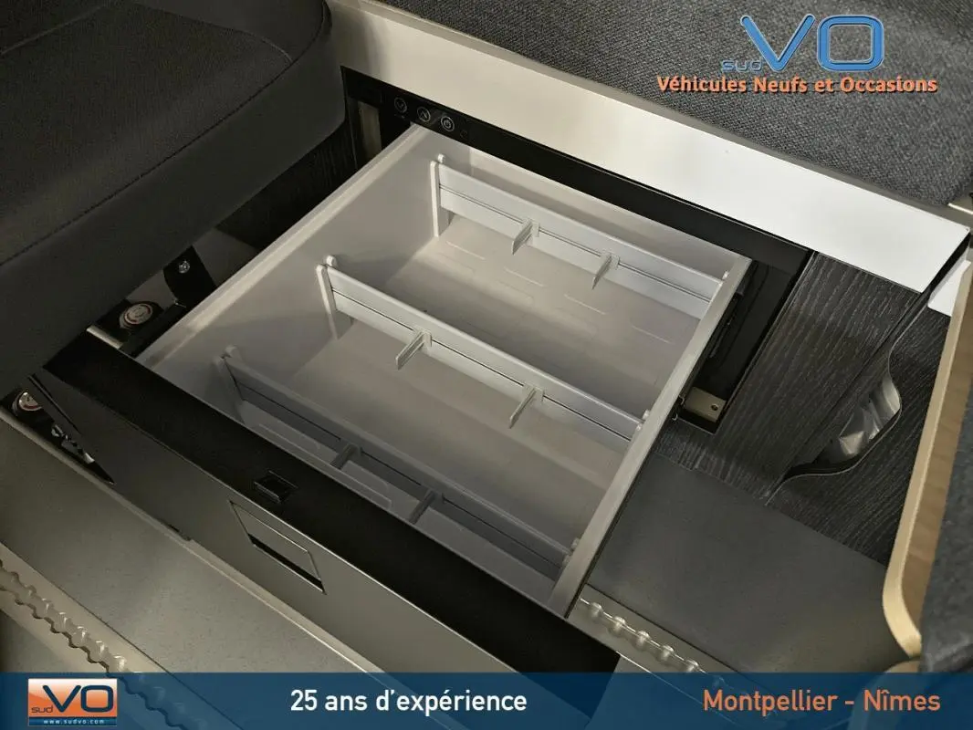 Tiroir de rangement ouvert sous siège dans l'habitacle du Renault Trafic Fourgon gris, version Confort 2025.