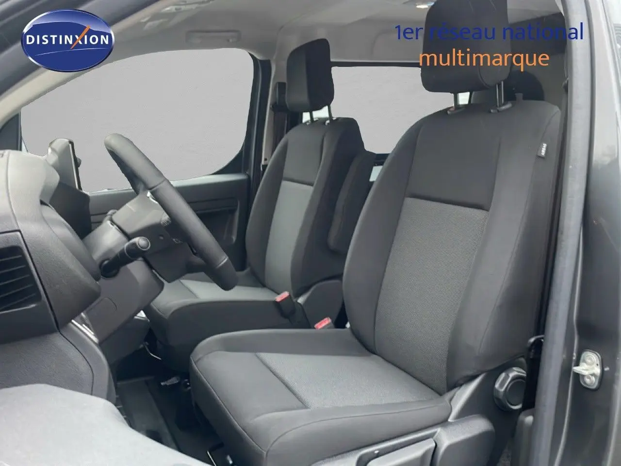 Vue intérieure côté conducteur du Citroën Jumpy Long L3 gris titane, montrant les sièges avant en tissu et cuir noir.