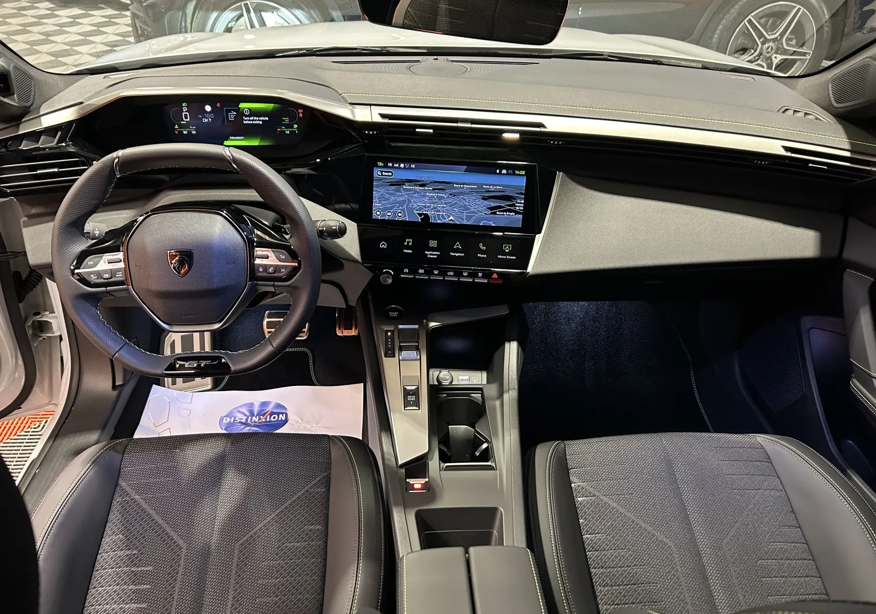 Vue intérieure frontale du poste de conduite de la Peugeot 308 HYBRID 145 GT, avec tableau de bord numérique et écran tactile GPS.