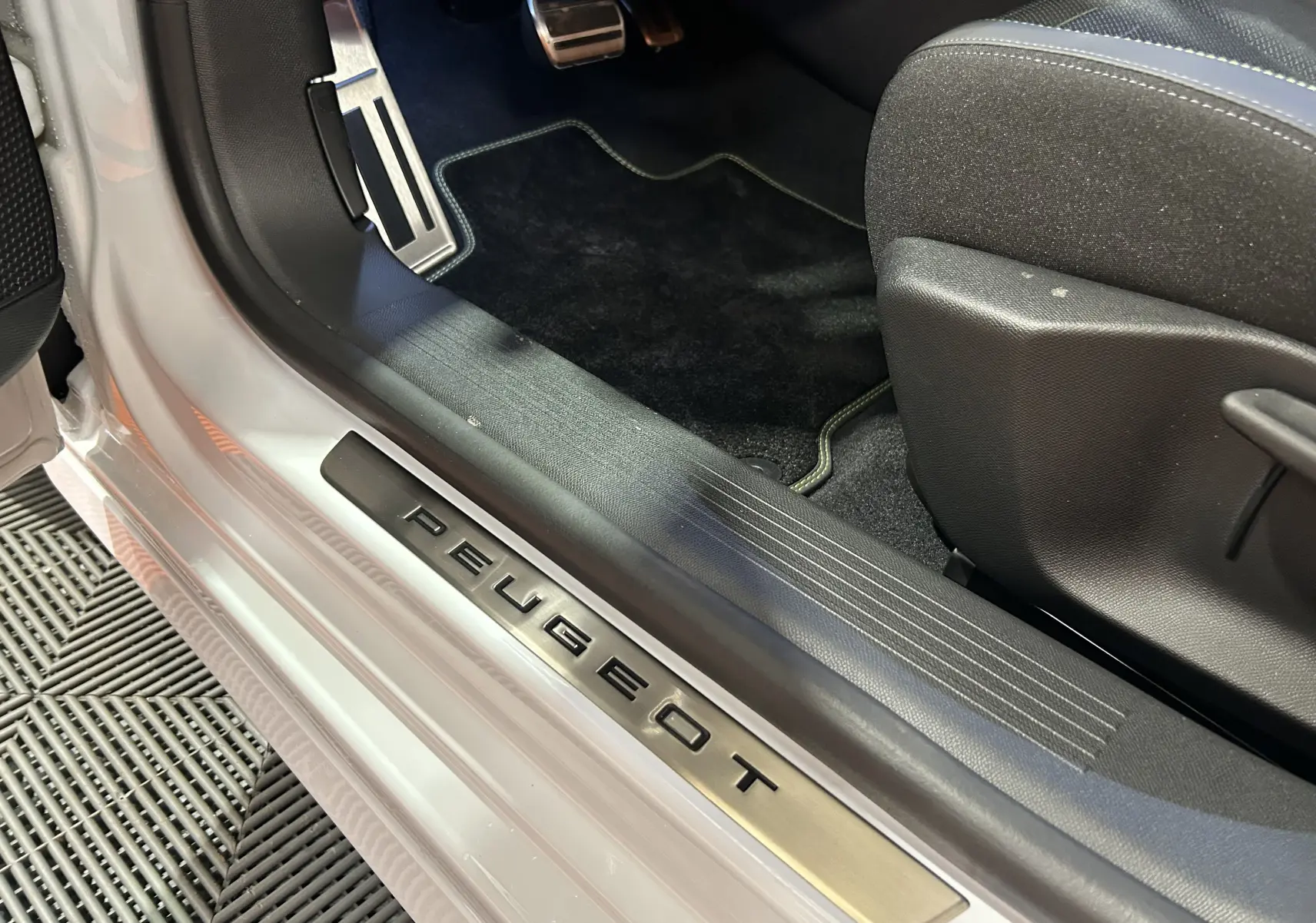 Gros plan sur la porte côté gauche d’une Peugeot 308 blanche, avec seuil de porte en métal marqué PEUGEOT.