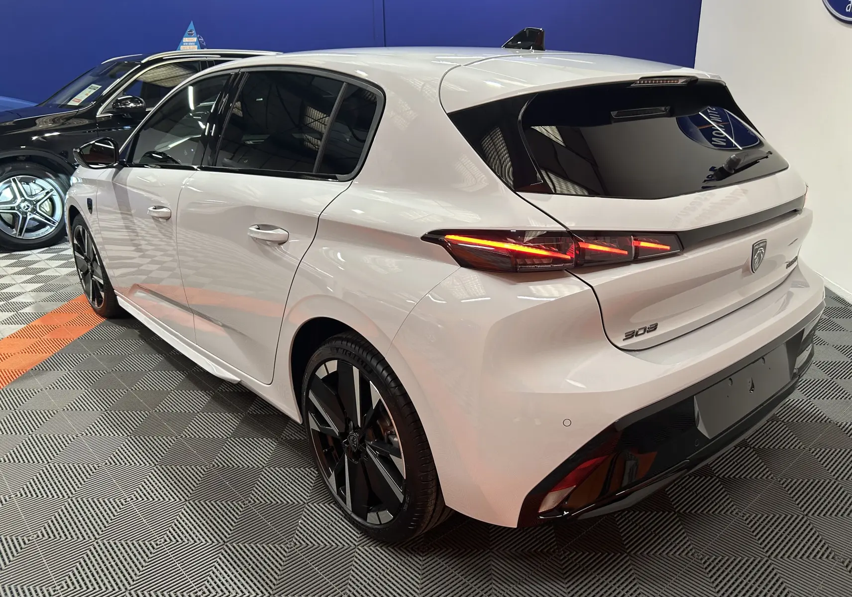 Vue 3/4 arrière droite d'une Peugeot 308 blanche Okenite avec feux LED distinctifs et jantes noires brillantes.