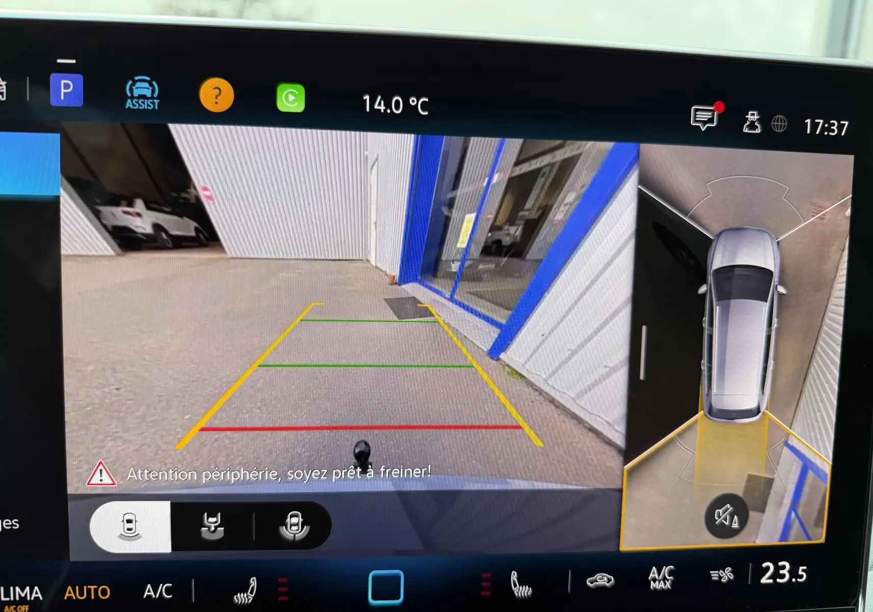 Vue écran caméra de recul et vue aérienne d'une Volkswagen Golf SW gris lunaire en marche arrière près d'un bâtiment.