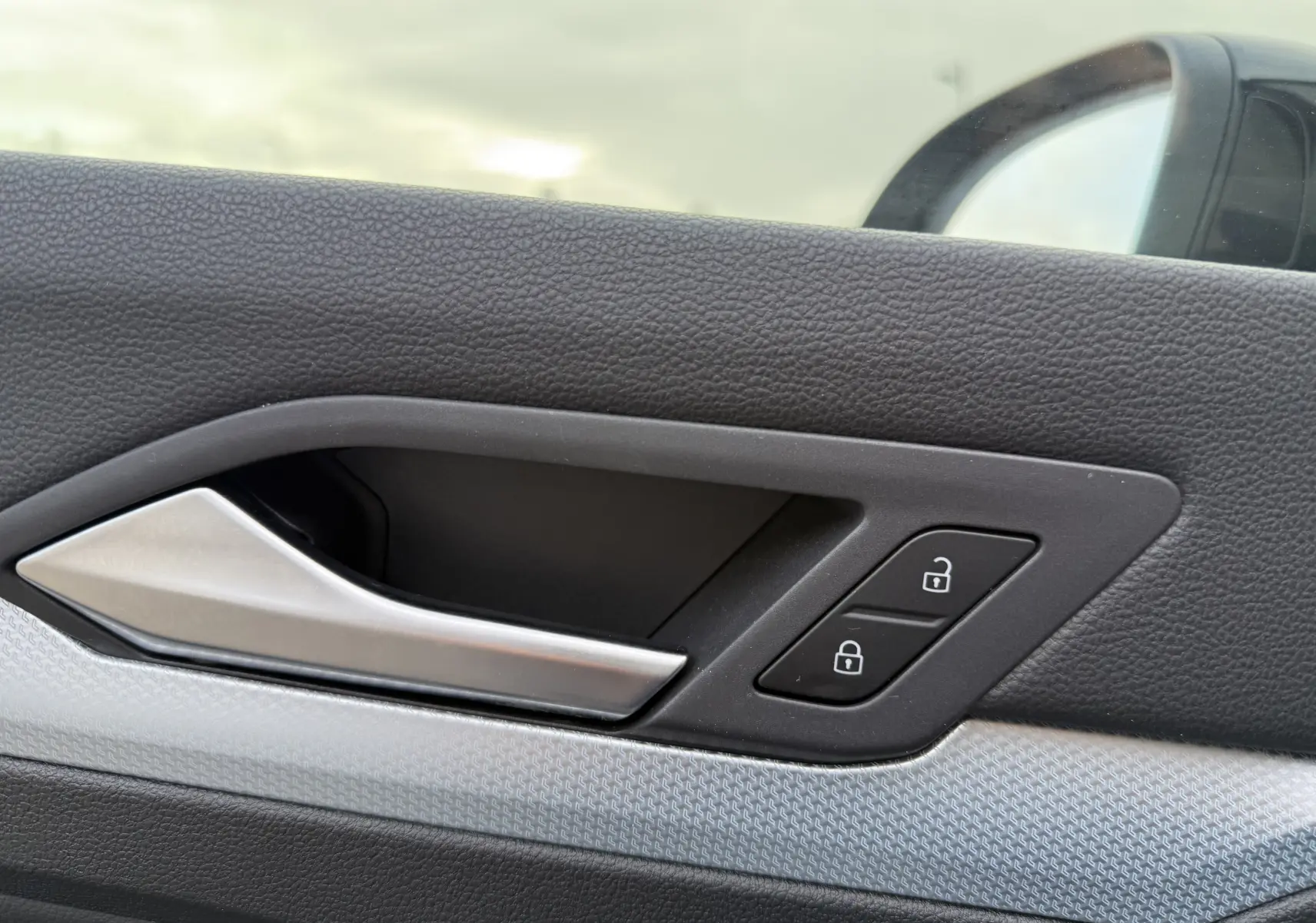 Poignée intérieure côté gauche de la porte d’une Volkswagen Golf SW gris lunaire avec boutons de verrouillage.