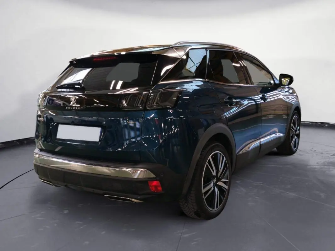 Vue 3/4 arrière droite d’un Peugeot 3008 Hybrid 225 e-EAT8 GT Pack bleu foncé avec jantes alliage 19 pouces et barres de toit.