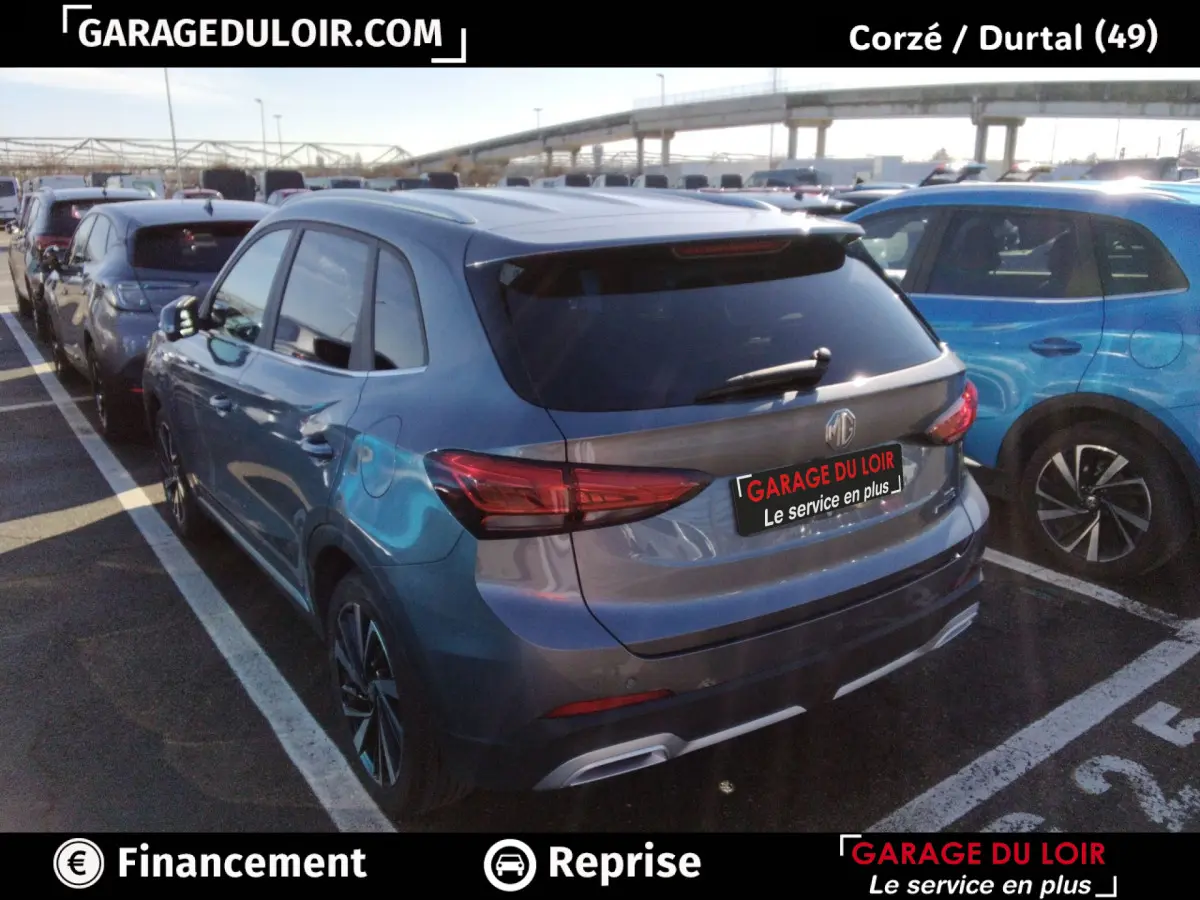 Vue 3/4 arrière droite d'un MG Motor ZS gris clair garé, avec feux arrière LED et toit ouvrant visible.