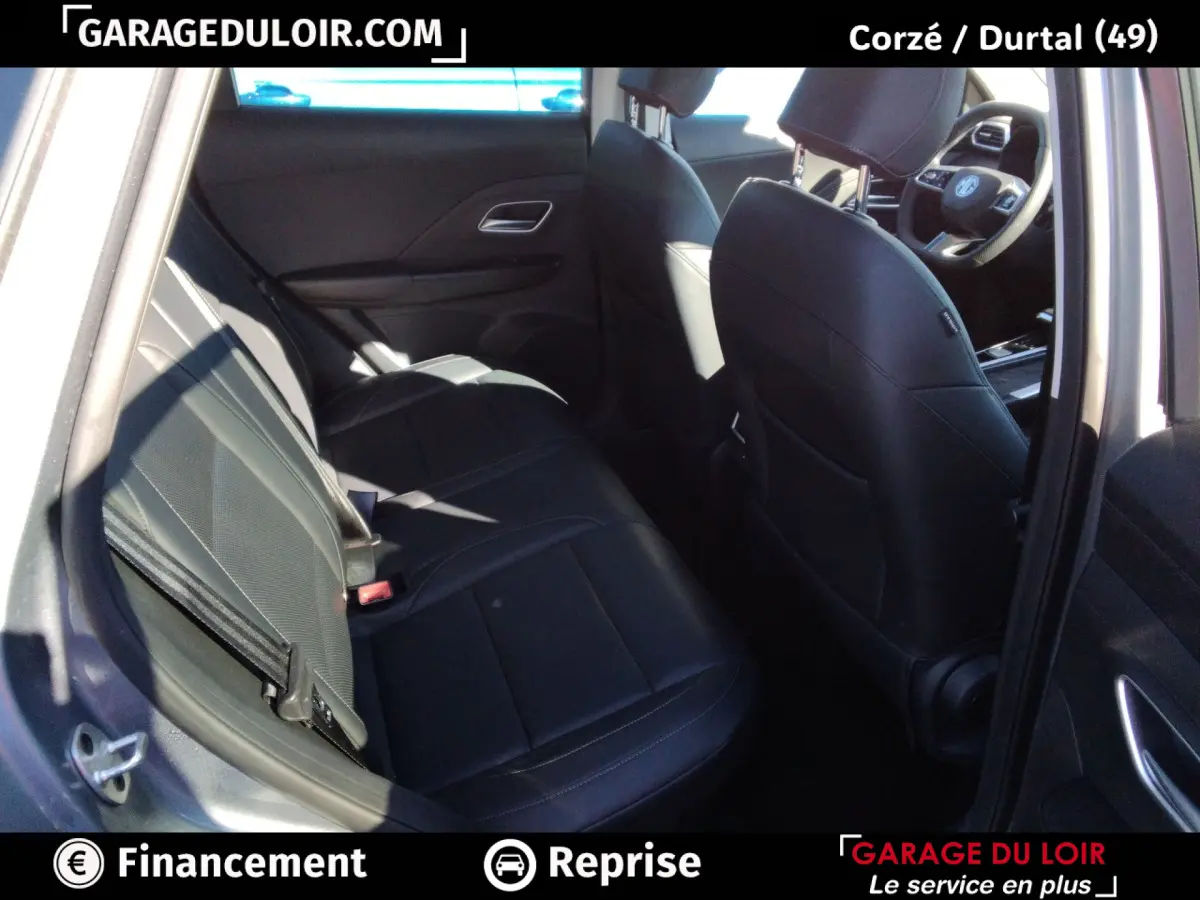 Vue intérieure côté arrière gauche du MG ZS 1.5L Hybrid+ Luxury 2025, sièges cuir noirs et tableau de bord partiel visible.