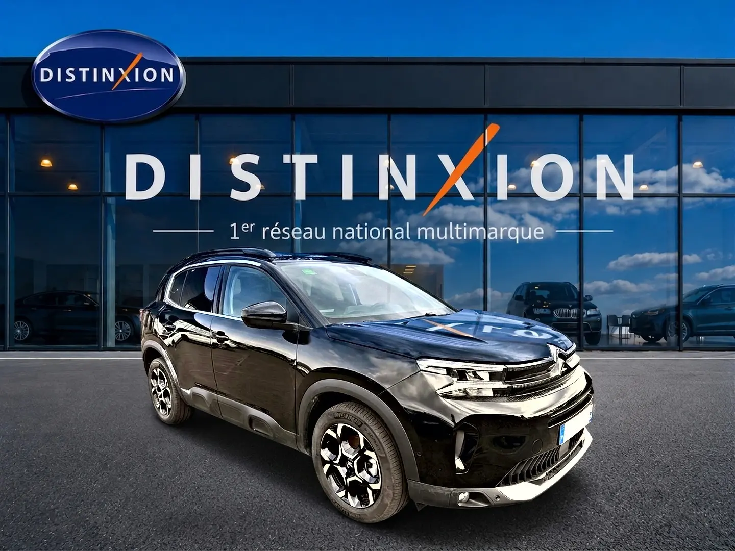 SUV Citroën C5 Aircross noir vu en 3/4 avant droit, avec jantes alu et barres de toit visibles devant un showroom.