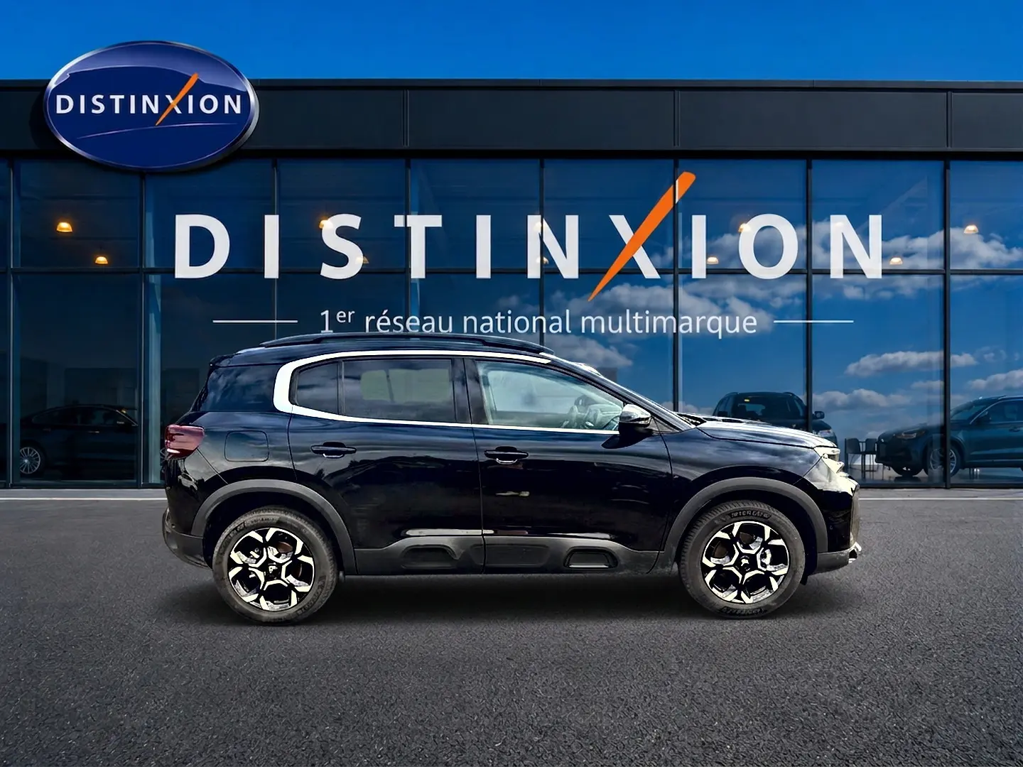 Profil droit d’un Citroën C5 Aircross noir 2025 avec jantes alu et barres de toit devant une vitrine Distinxion.