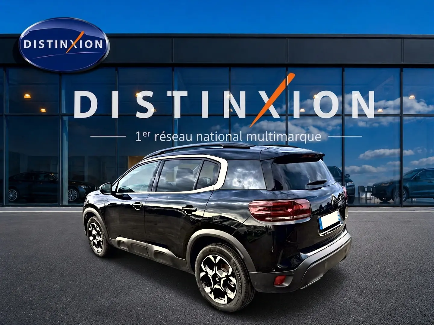 Vue 3/4 arrière droite d'un Citroën C5 Aircross noir brillant avec jantes alu et barres de toit visibles.