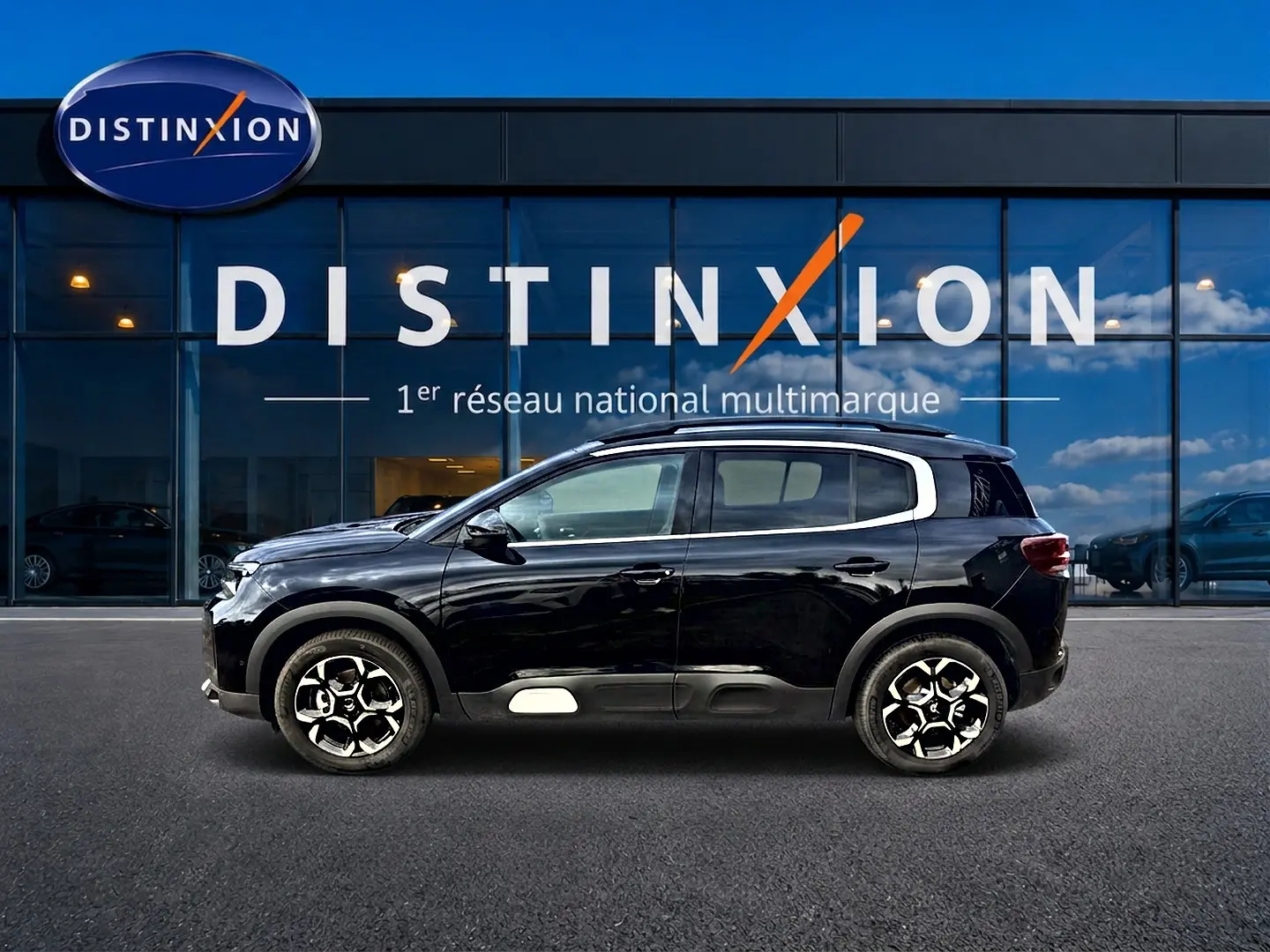 Profil droit d'un Citroën C5 Aircross noir 2025 avec jantes alu et barres de toit devant une vitrine Distinxion.