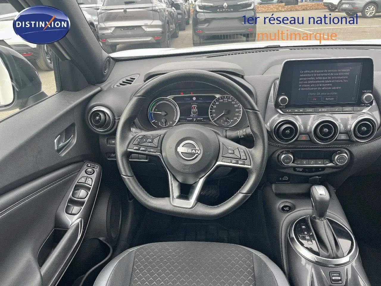 Vue intérieure avant du Nissan Juke 2024 blanc nacré, mettant en valeur le volant multifonction et l'écran tactile central.