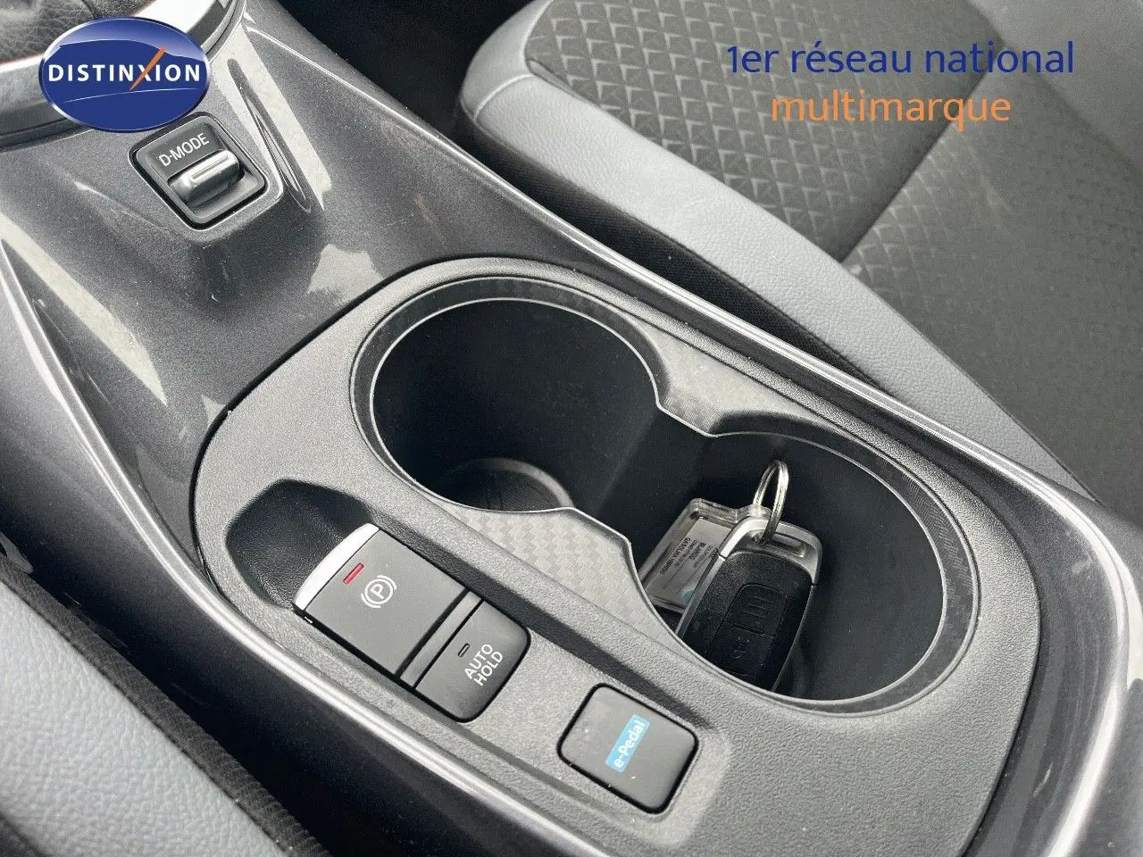 Gros plan sur la console centrale noire du Nissan Juke blanc nacré, avec porte-gobelets et clés posées.