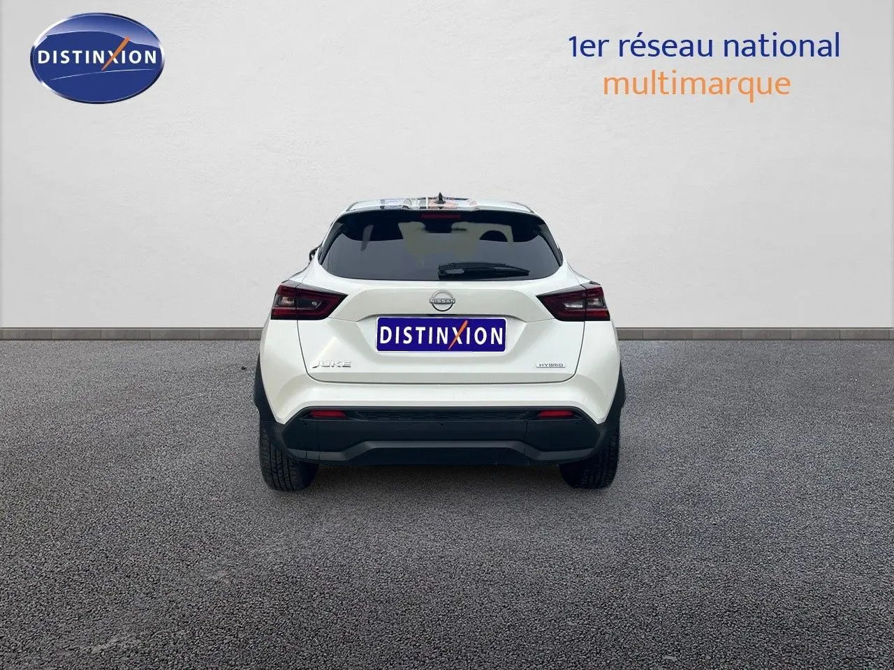 Vue arrière d'un Nissan Juke blanc nacré 2024 avec logo hybride et plaque Distinxion visible.