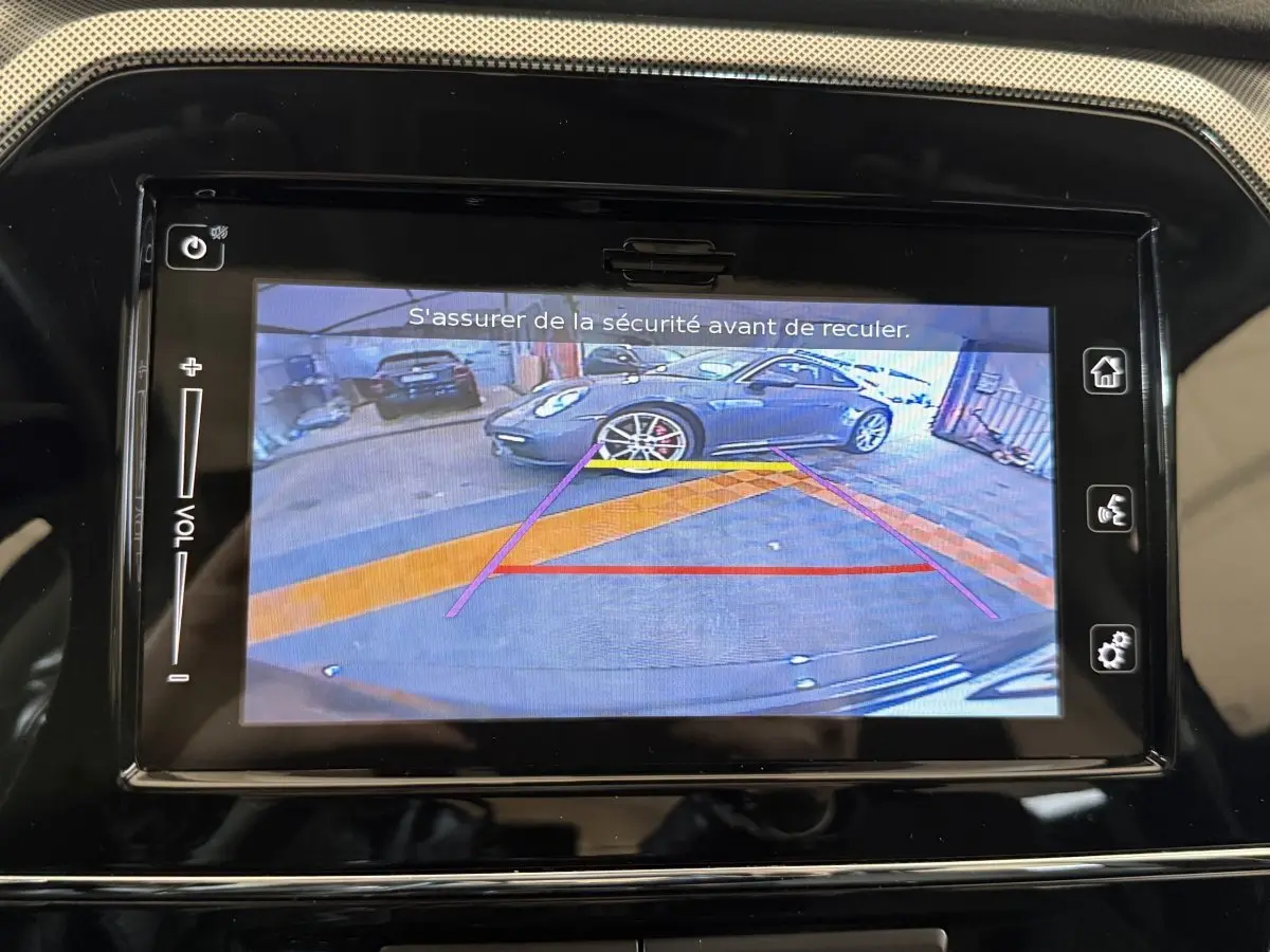 Écran tactile montrant la caméra de recul avec vue arrière d’un véhicule gris stationné en intérieur.