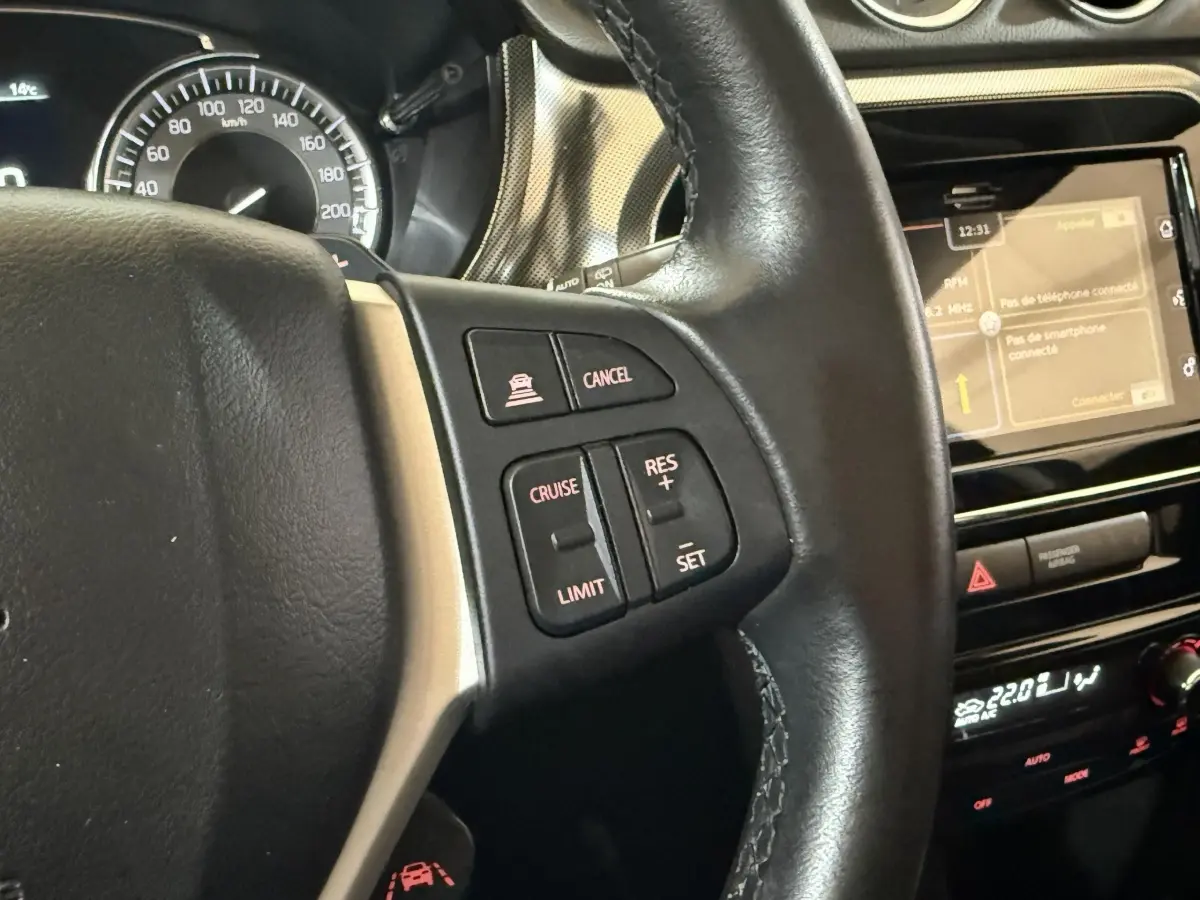 Vue rapprochée du volant noir de la Suzuki Vitara 2022, avec commandes de régulateur et écran tactile du tableau de bord visible.