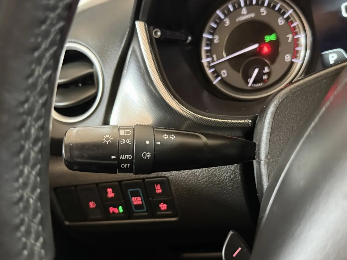 Gros plan sur la manette des phares et les boutons de contrôle du tableau de bord du Suzuki Vitara 1.5 Hybrid noir, intérieur.