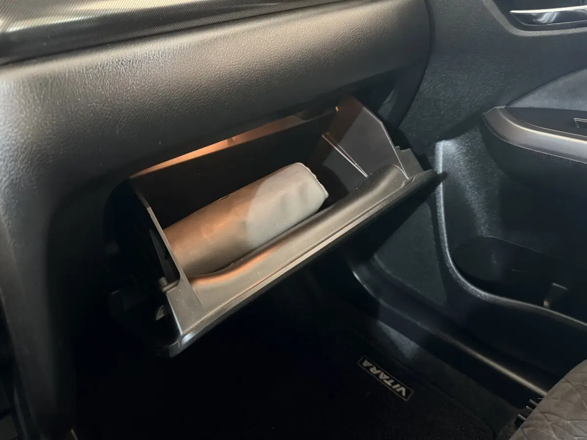 Gros plan sur la boîte à gants ouverte côté passager du Suzuki Vitara noir, avec un objet beige à l'intérieur.