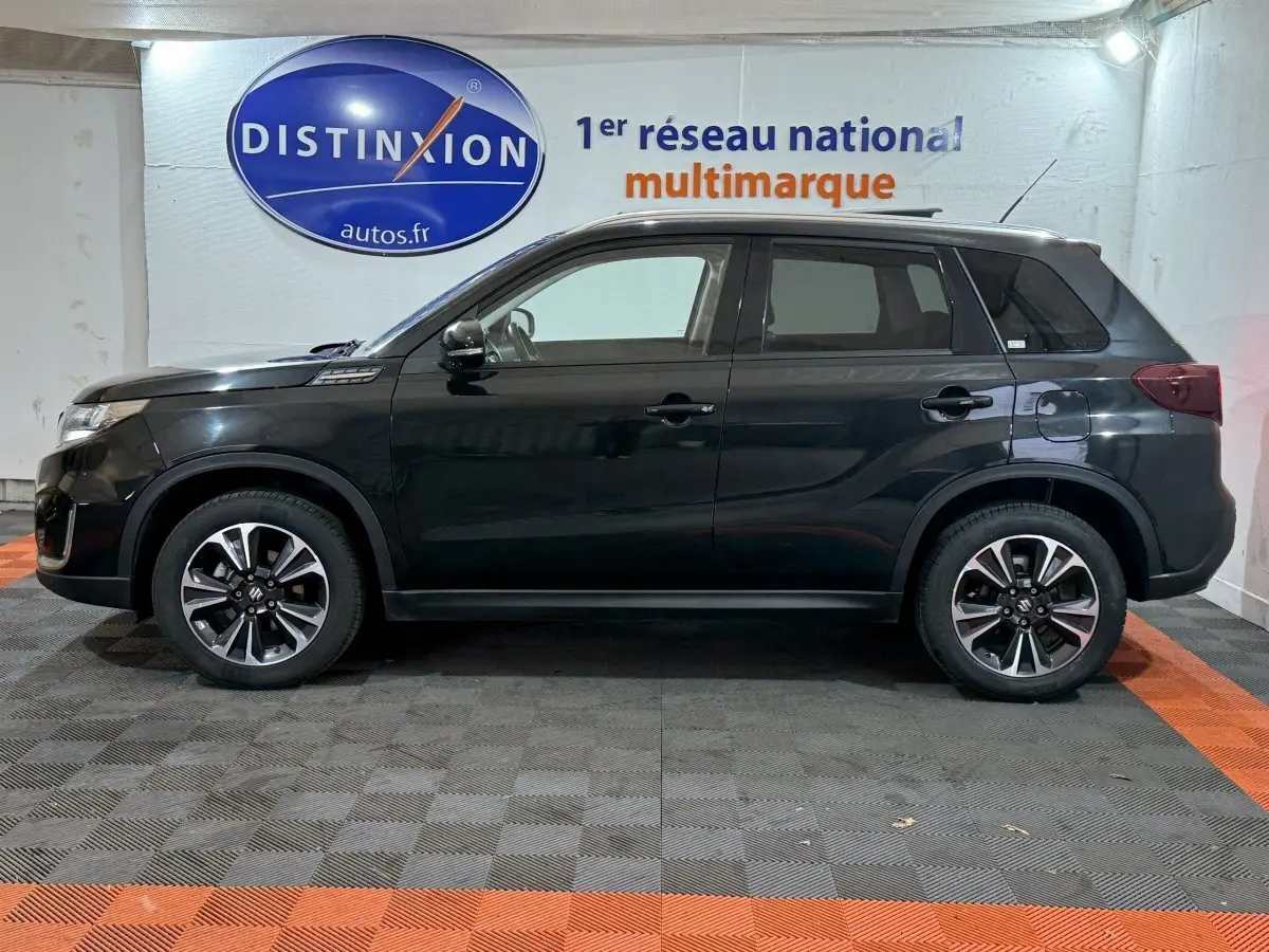 Profil côté gauche du Suzuki Vitara noir 2022 dans un showroom avec jantes alliage et vitres teintées.