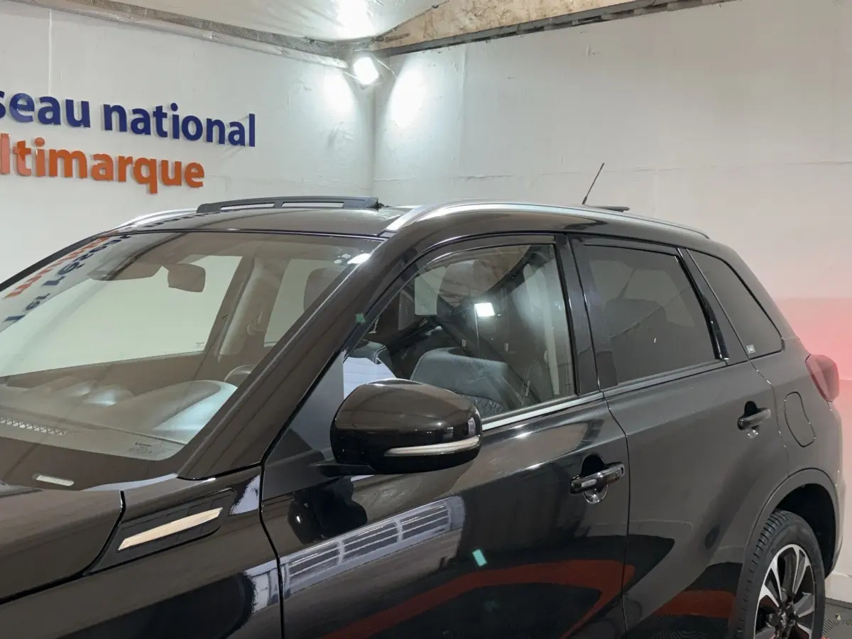 Vue de profil côté gauche d'un Suzuki Vitara noir 2022 avec rétroviseur et barres de toit visibles.