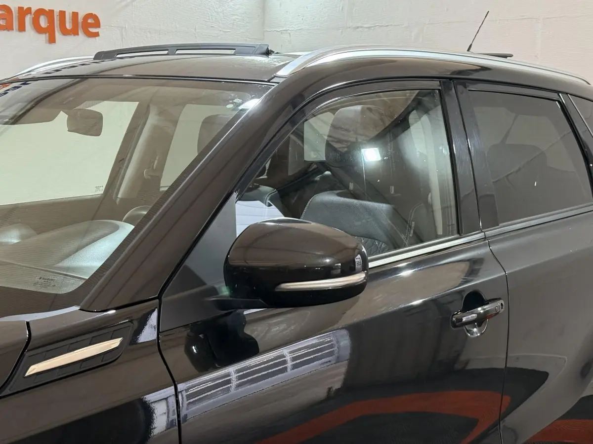 Vue latérale côté gauche du Suzuki Vitara noir 2022 avec rétroviseur et toit ouvrant en verre visibles.