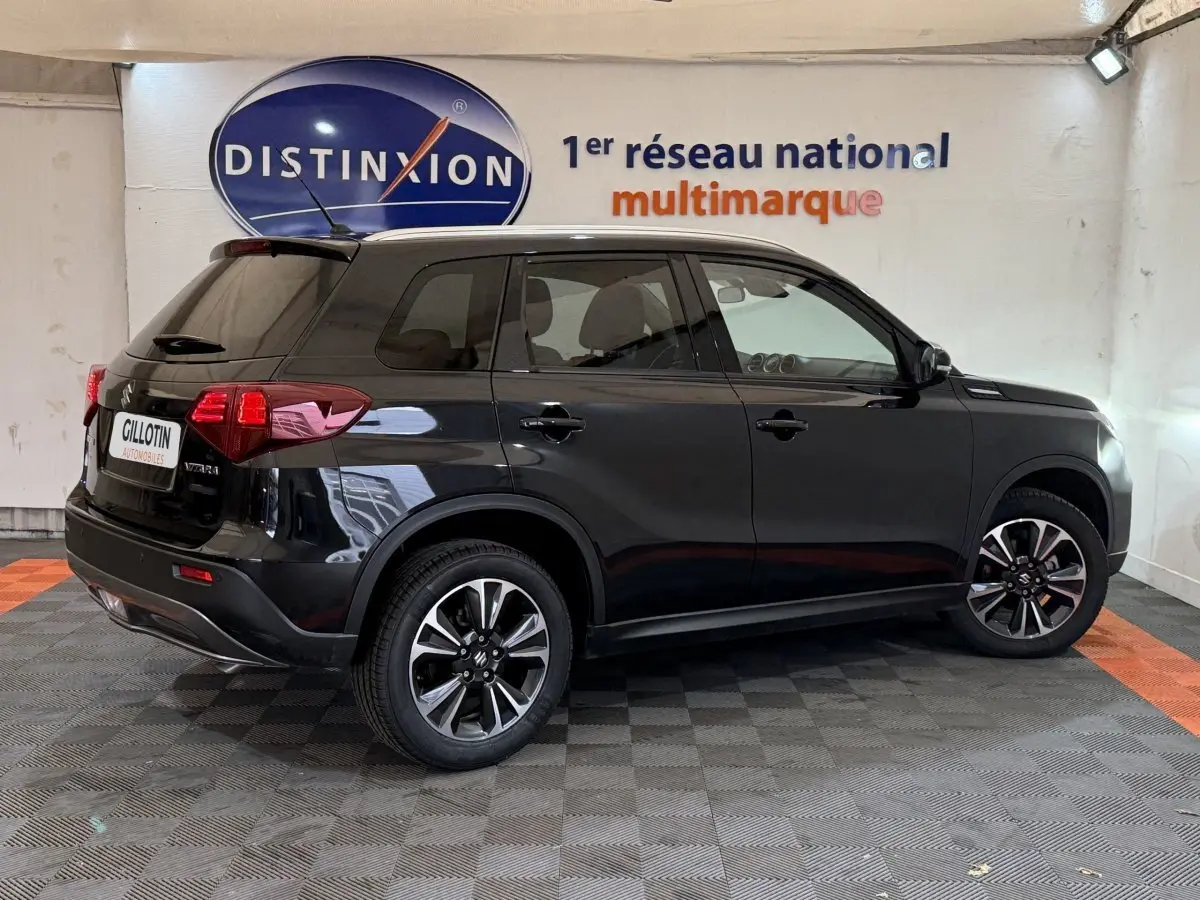 Suzuki Vitara noir vu de profil côté droit dans un showroom avec jantes alliage et vitres teintées.
