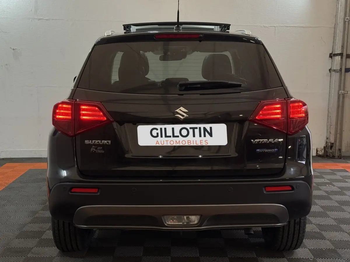 Vue arrière d'un Suzuki Vitara noir 2022 avec feux allumés et logo hybride visible sur le hayon.