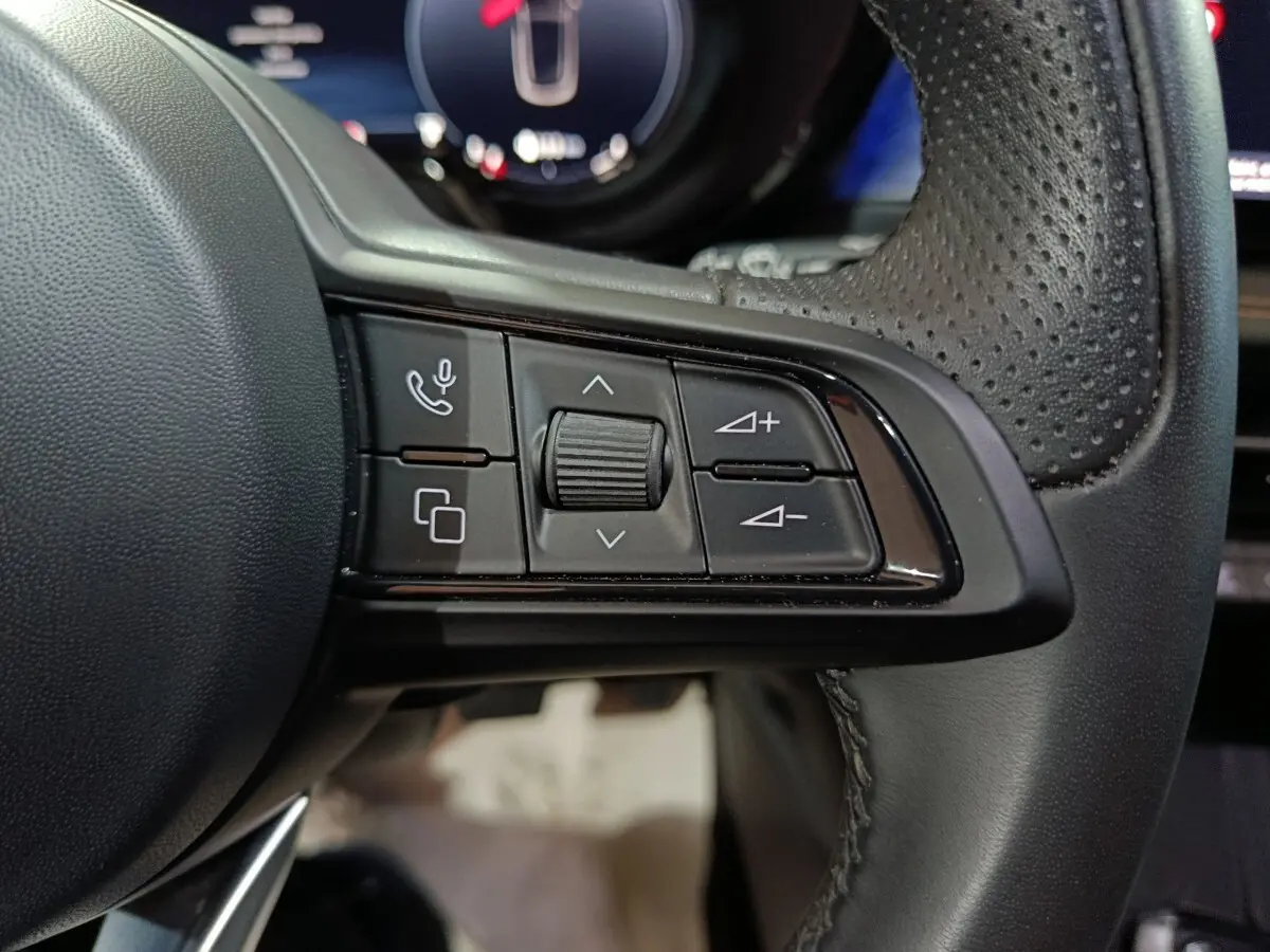 Gros plan sur les commandes multifonctions à gauche du volant en cuir perforé de l'Alfa Romeo Tonale bleu.