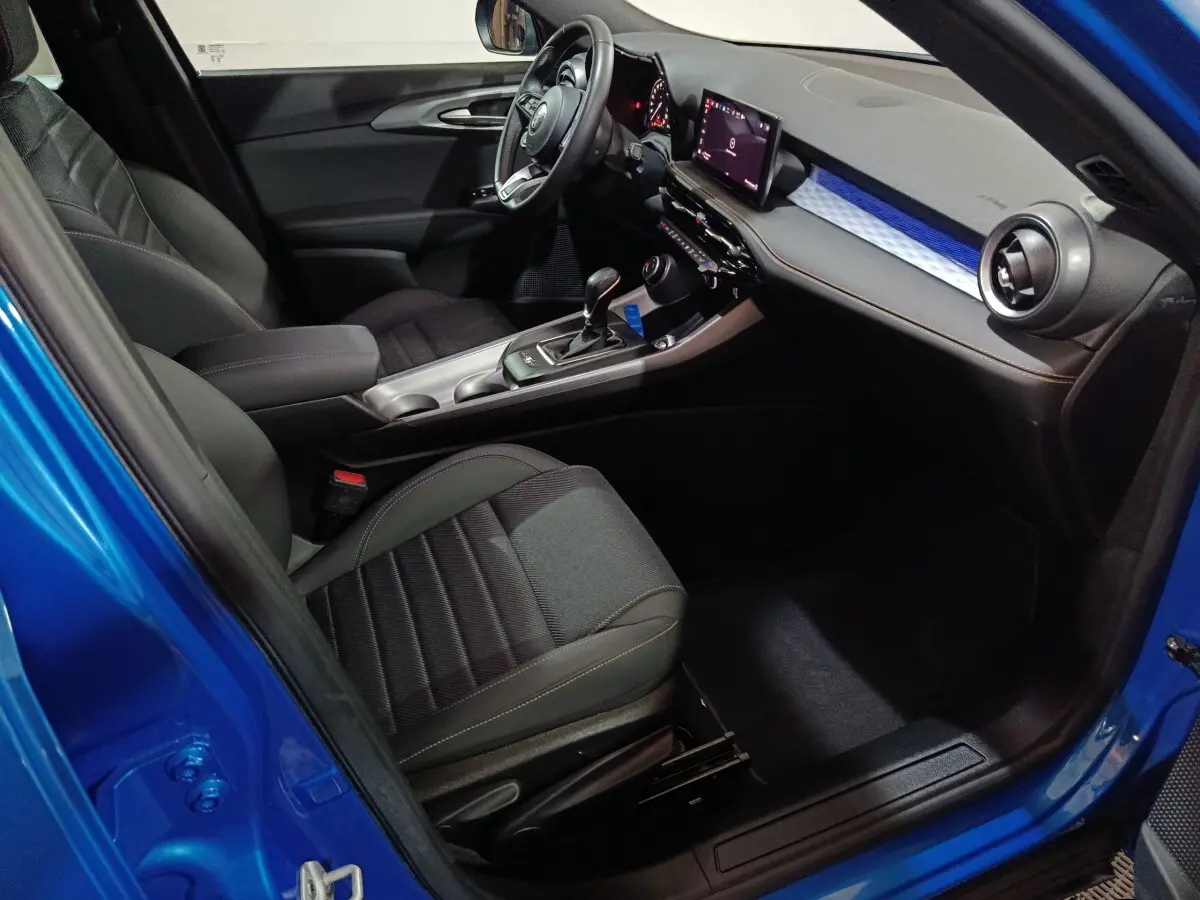 Vue intérieure côté conducteur de l'Alfa Romeo Tonale bleu, avec tableau de bord digital et sièges noirs.