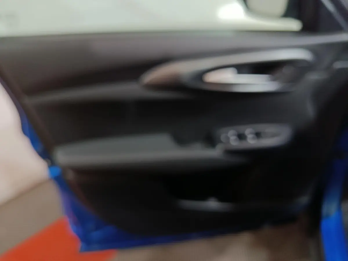 Vue intérieure de la porte avant gauche d'une Alfa Romeo Tonale bleu, avec poignée et commandes de vitres visibles.