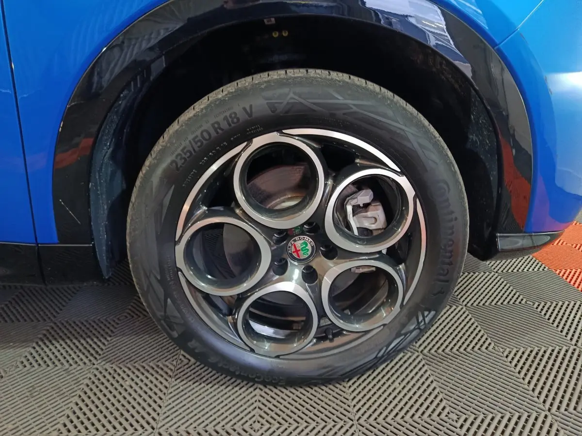 Gros plan sur la roue avant gauche d'une Alfa Romeo Tonale bleu, avec jante distinctive à cinq cercles.