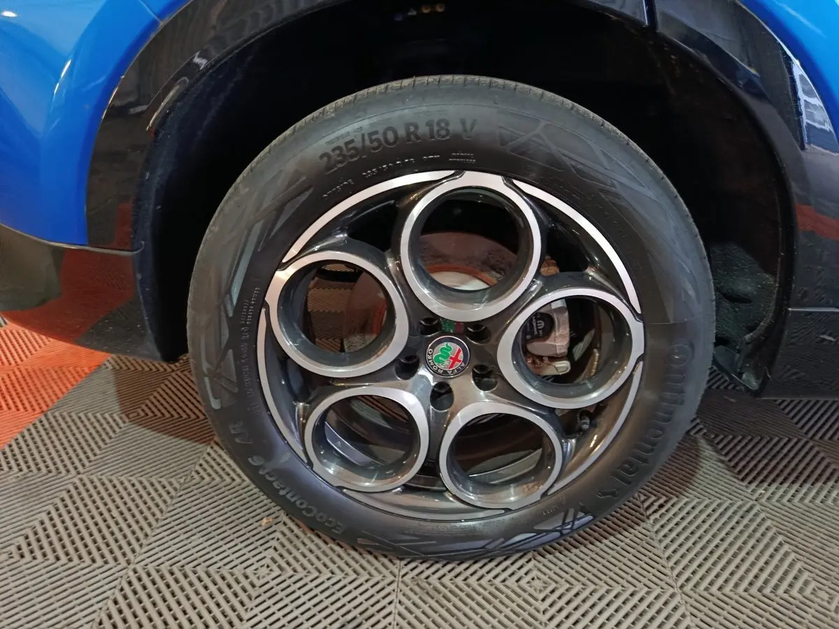 Gros plan sur la roue arrière droite d'une Alfa Romeo Tonale bleu 2023, avec passage de roue noir brillant.