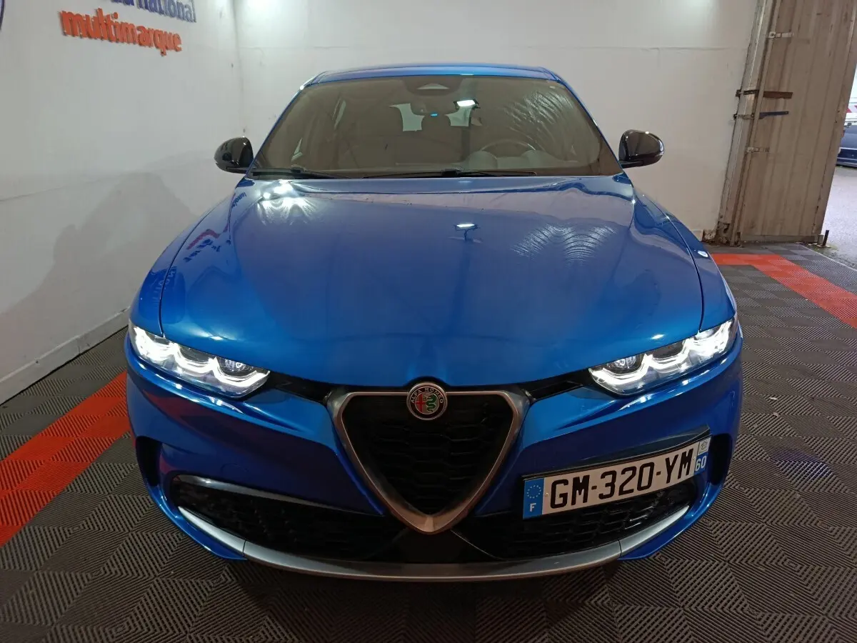 Vue avant d'une Alfa Romeo Tonale bleu électrique avec phares allumés et calandre caractéristique en V.
