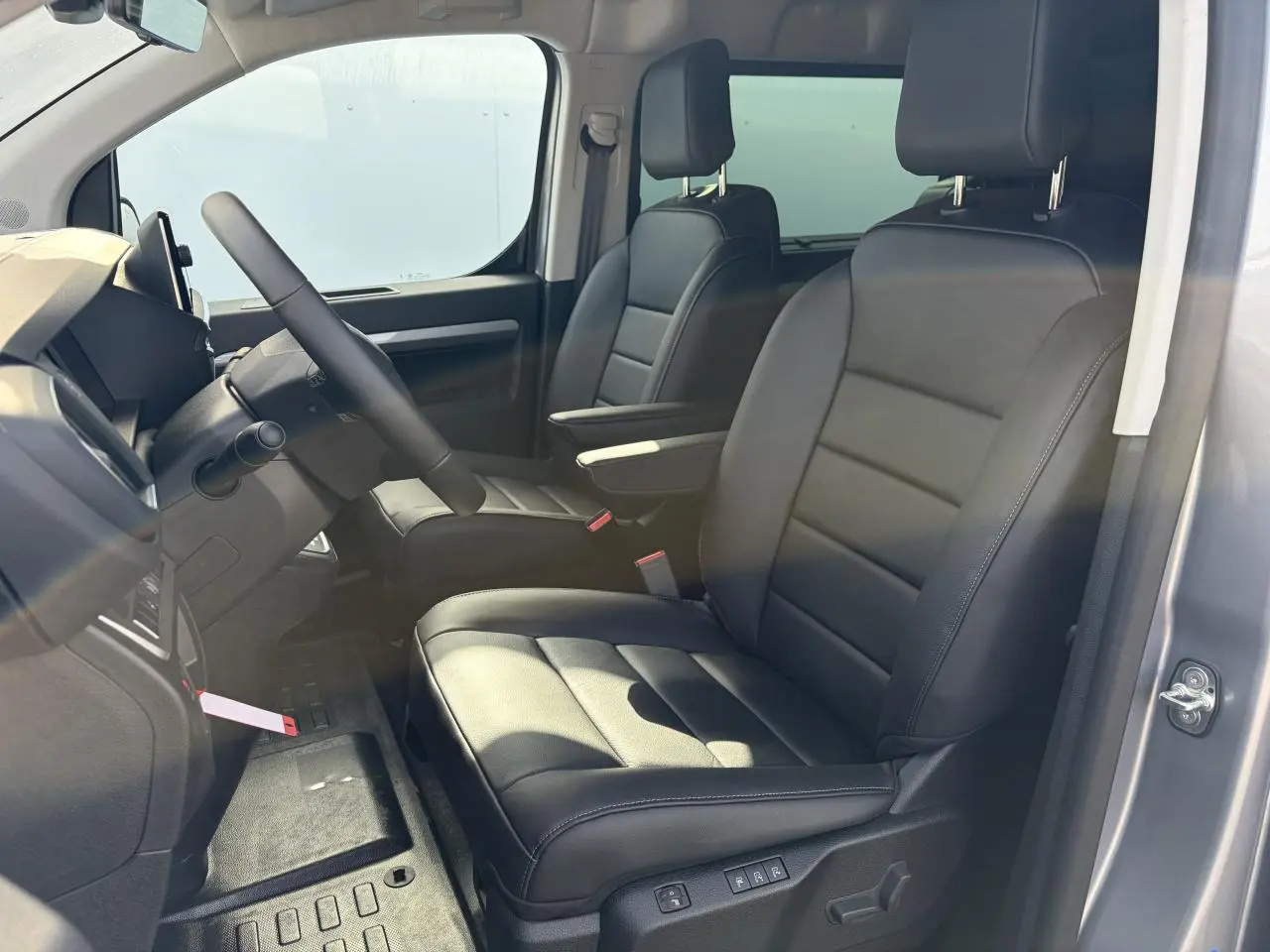 Vue intérieure côté conducteur du Citroën Jumpy gris acier, sièges cuir noirs avec accoudoirs et volant chauffant.