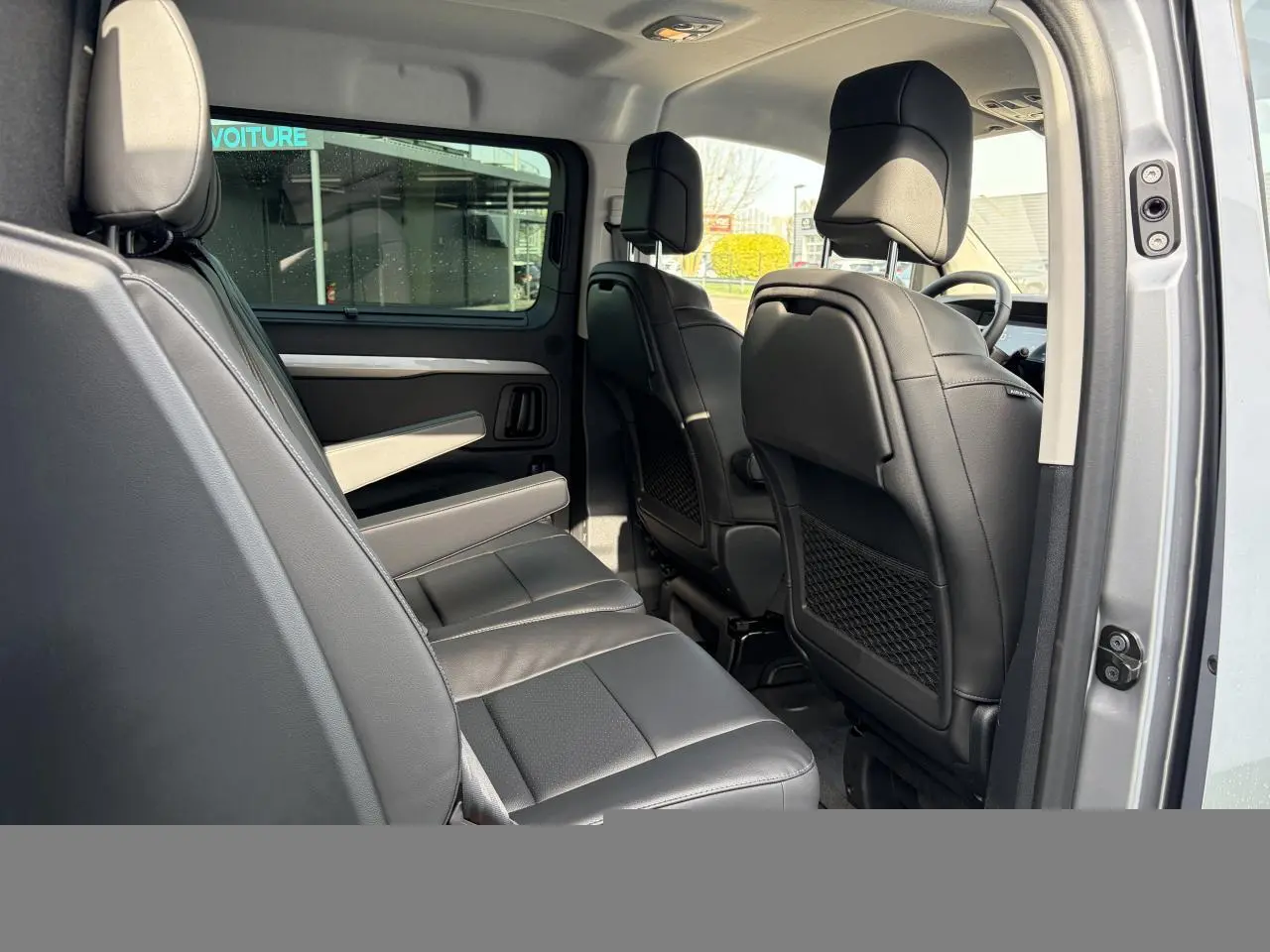 Vue intérieure côté gauche du Citroën Jumpy gris acier, montrant la banquette arrière en cuir et les sièges avant noirs.