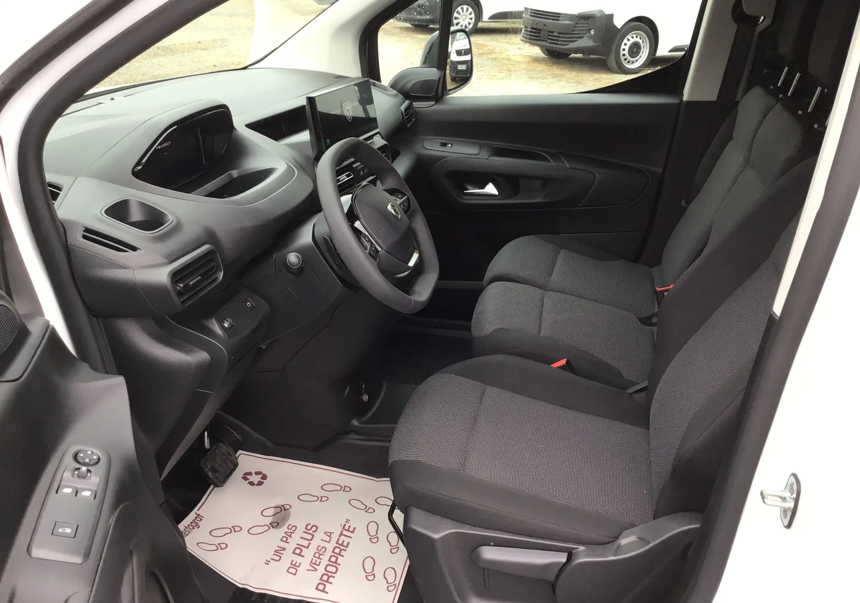 Vue intérieure côté conducteur du Peugeot Partner blanc 2026, montrant les sièges avant et le tableau de bord moderne avec écran tactile.