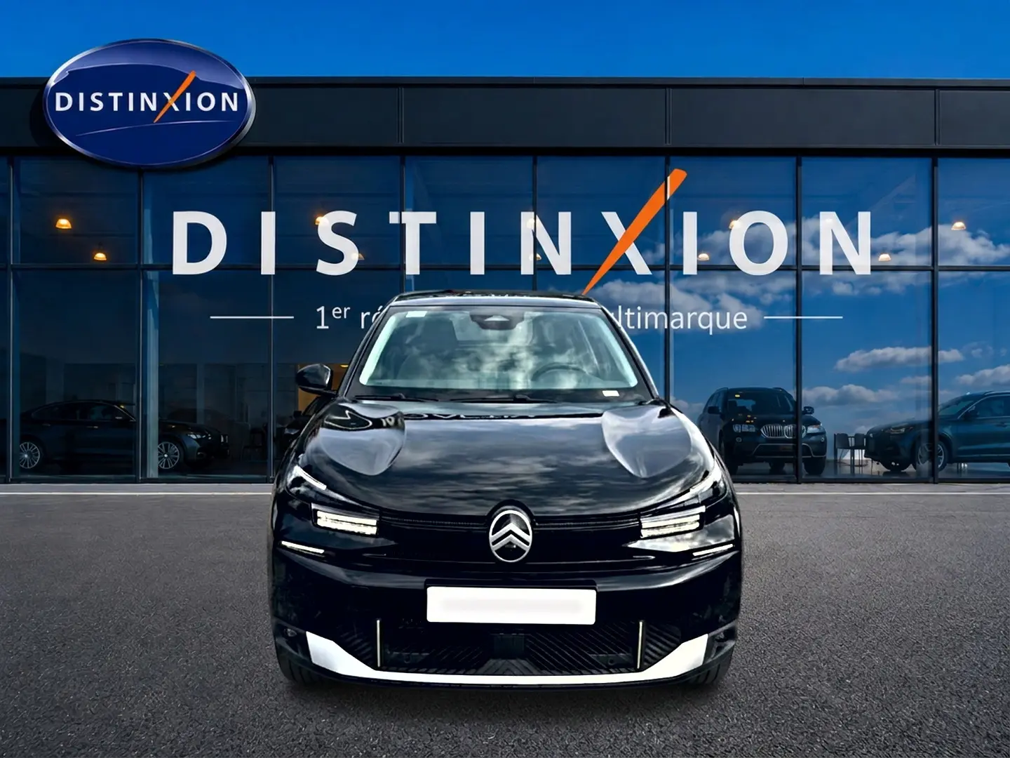 Vue frontale d'une Citroën C4 X noire 2025 avec calandre distinctive et phares LED fins, devant une vitrine Distinxion.