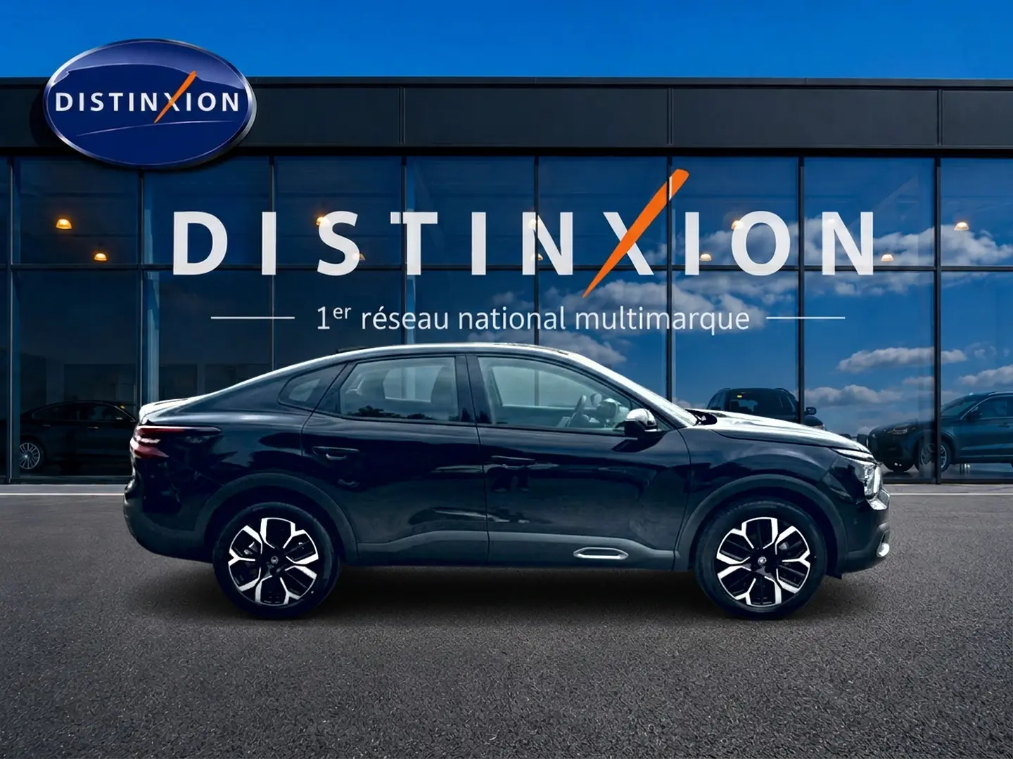 Profil côté gauche de la Citroën C4 X noire 2025 avec jantes alu et lignes fluides devant une vitrine Distinxion.
