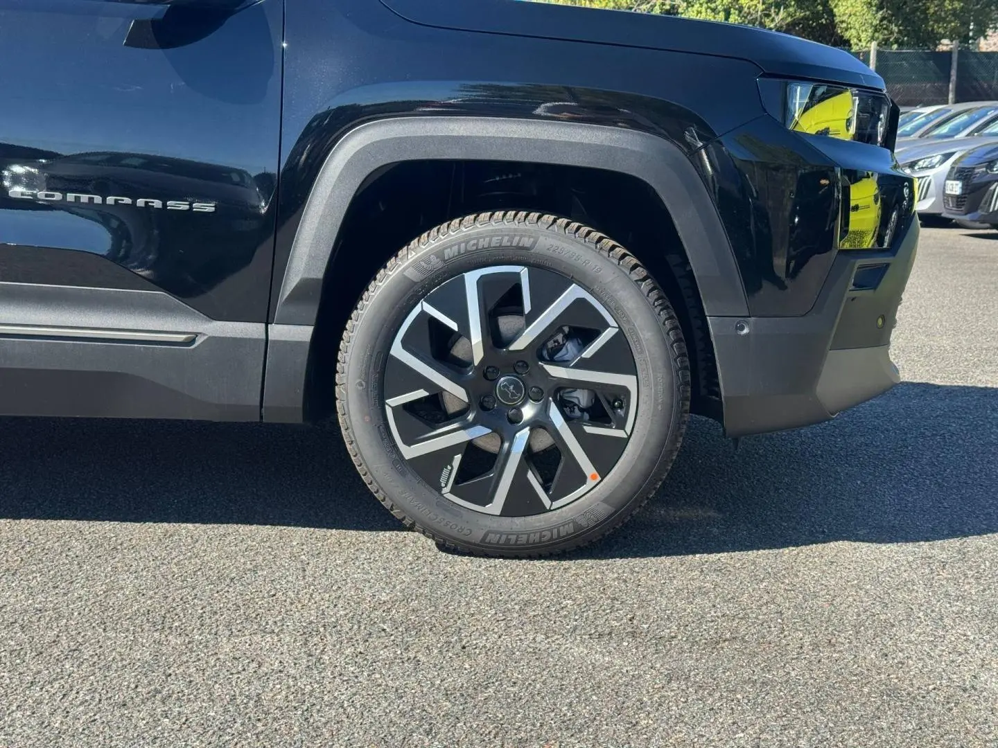 Gros plan sur la roue avant gauche du Jeep Compass Vulcano 2026 avec jante alu et logo Jeep visible sur la carrosserie noire.