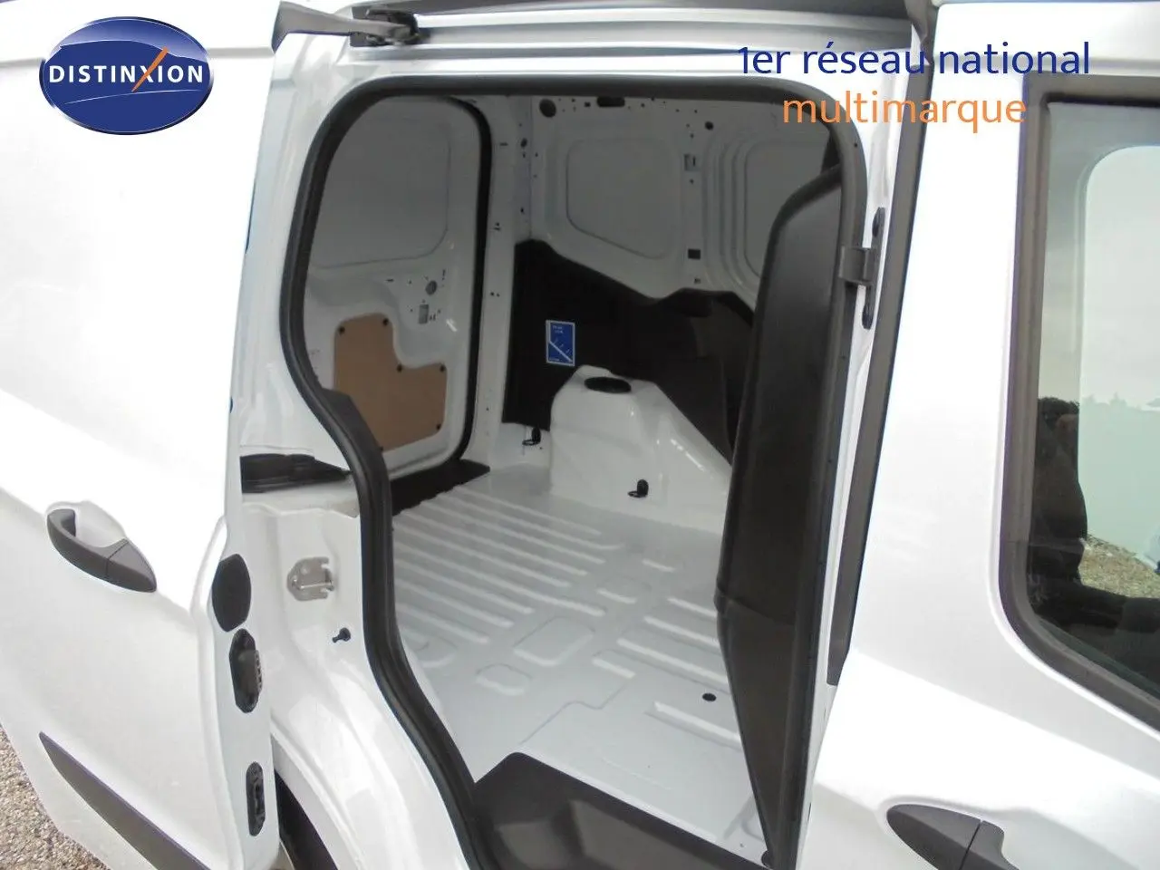 Vue intérieure du fourgon Ford Transit Courier blanc glacier, montrant l'espace de chargement vide avec porte latérale ouverte.