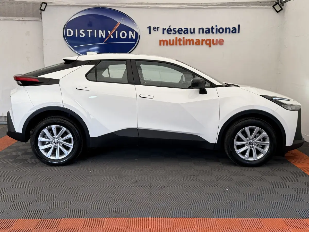 Profil côté droit d’un Toyota C-HR blanc 2024 avec jantes alliage et détails noirs contrastants sur les bas de caisse.