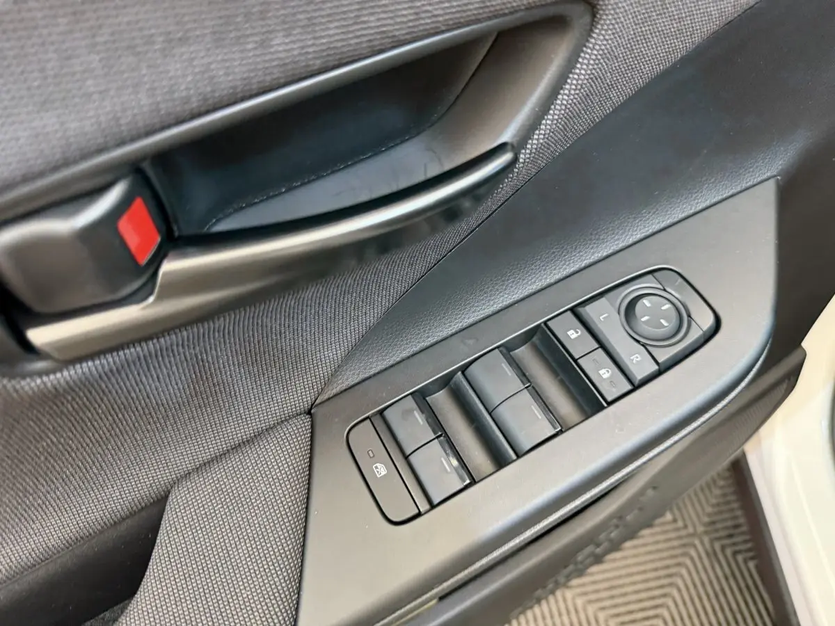 Détail de la porte côté conducteur du Toyota C-HR blanc 2024, avec commandes électriques des vitres et rétroviseurs.