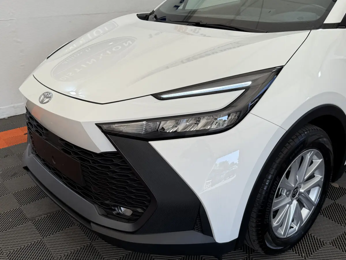 Vue 3/4 avant droit du Toyota C-HR 1.8 Hybride 140 Dynamic blanc avec phares LED et calandre noire texturée.