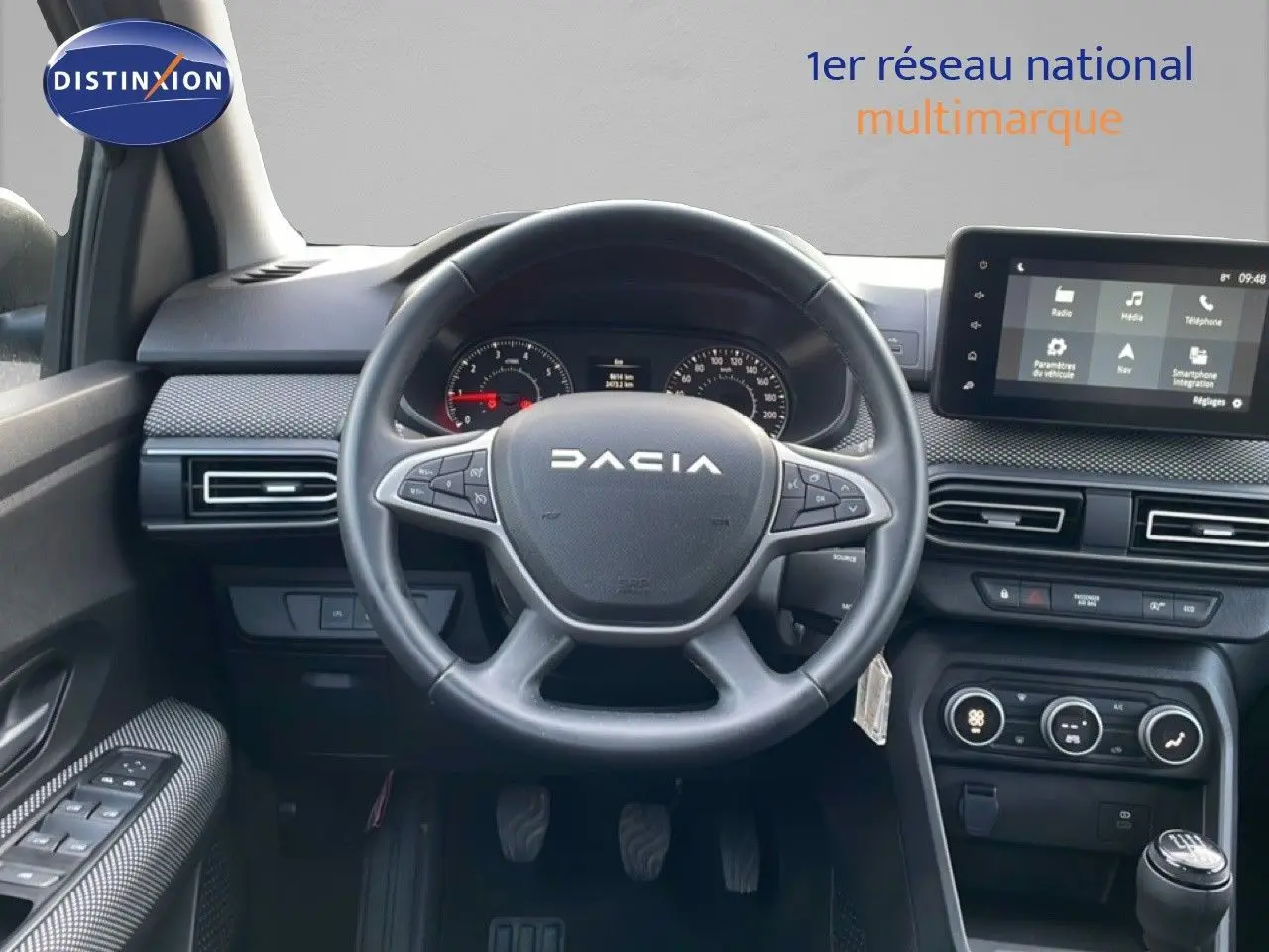Vue intérieure centrée sur le volant DACIA et le tableau de bord avec écran tactile, ambiance sobre en gris et noir.