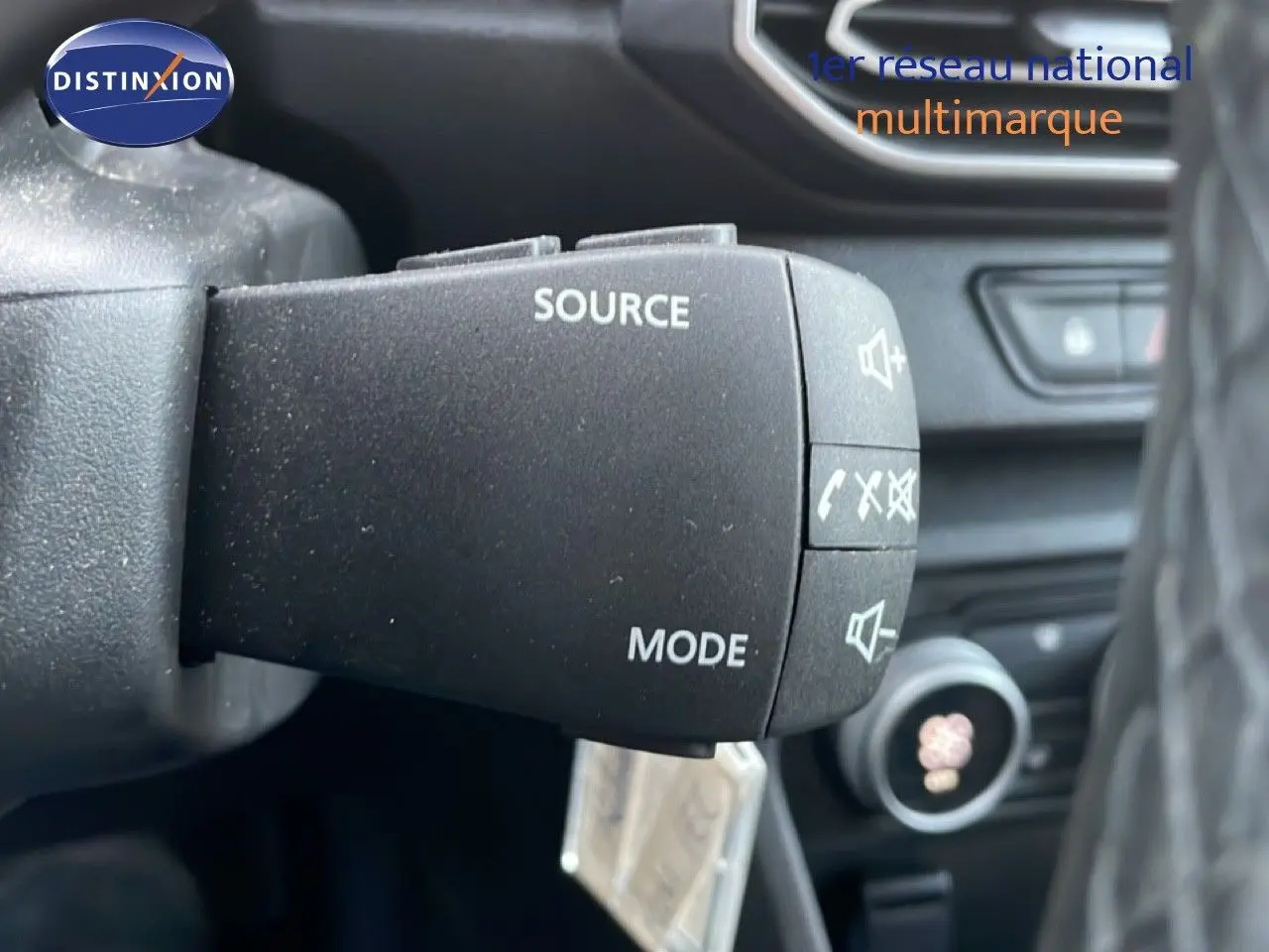 Gros plan sur la commande au volant du Dacia Jogger 2025, boutons source et mode visibles dans l'habitacle noir.