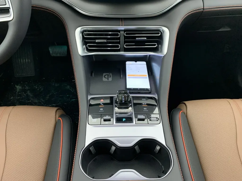 Vue plongeante sur la console centrale du BYD SEAL U 2025 Time Grey, avec levier de vitesses, chargeur sans fil et sièges marron à surpiqûres orange.