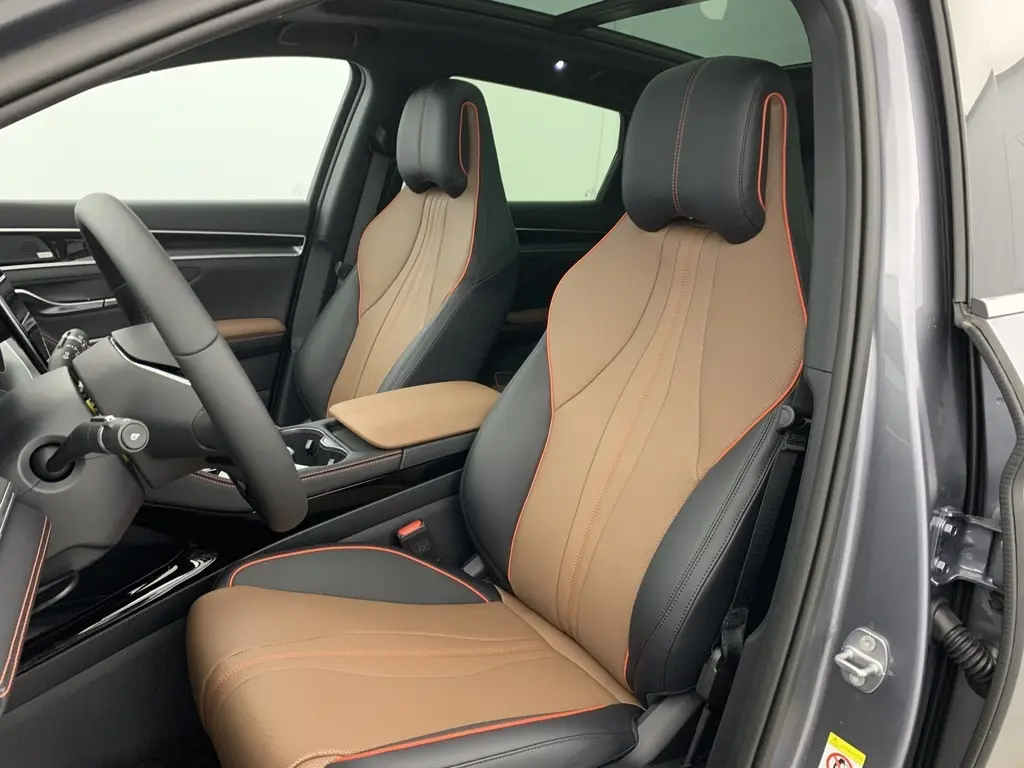 Vue intérieure côté conducteur du BYD SEAL U 2025 avec sièges en similicuir bicolore noir et marron, surpiqûres orange et toit ouvrant panoramique.